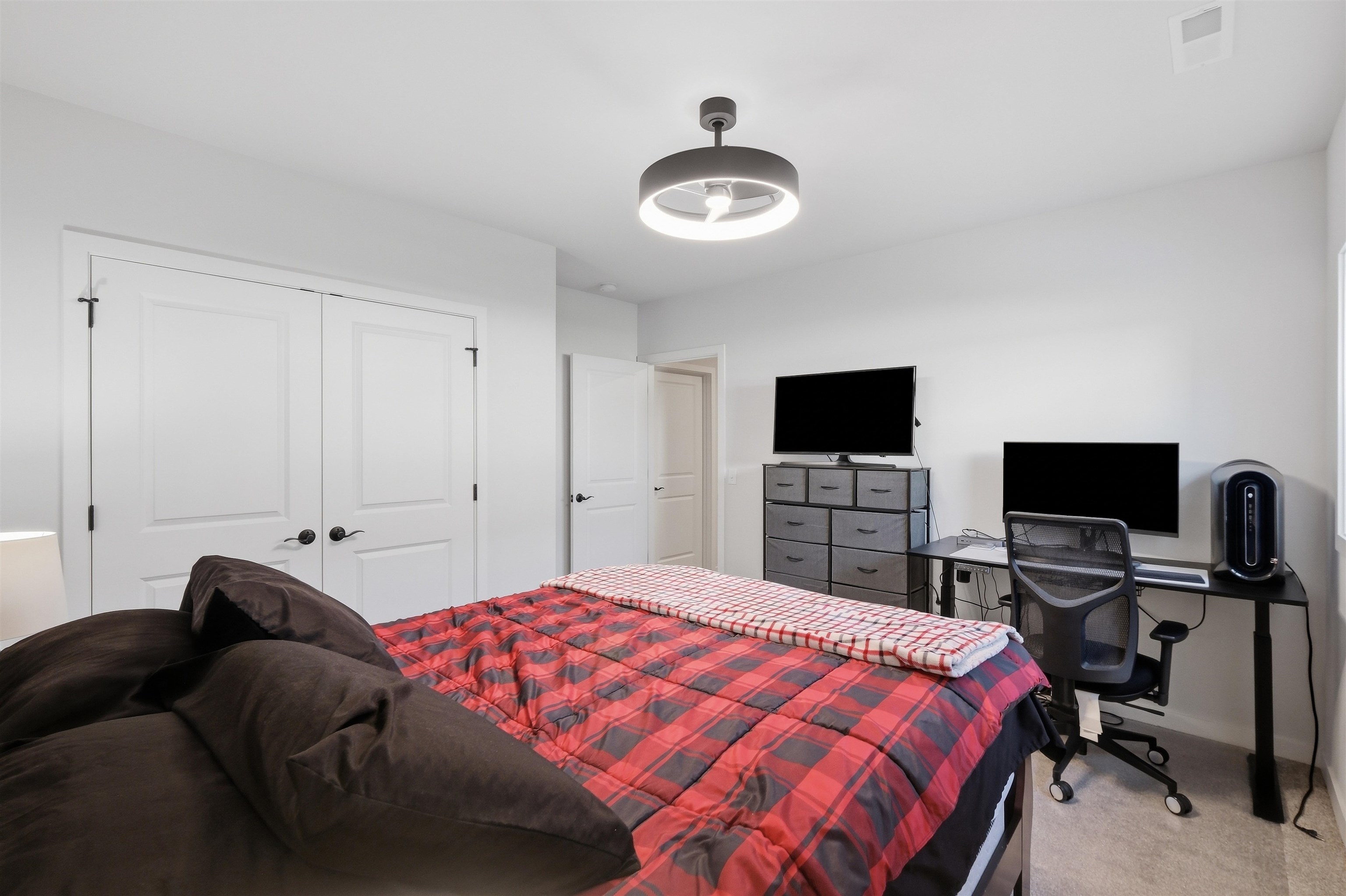 Bedroom with a red plaid bedspread and computer workstation with two monitors.