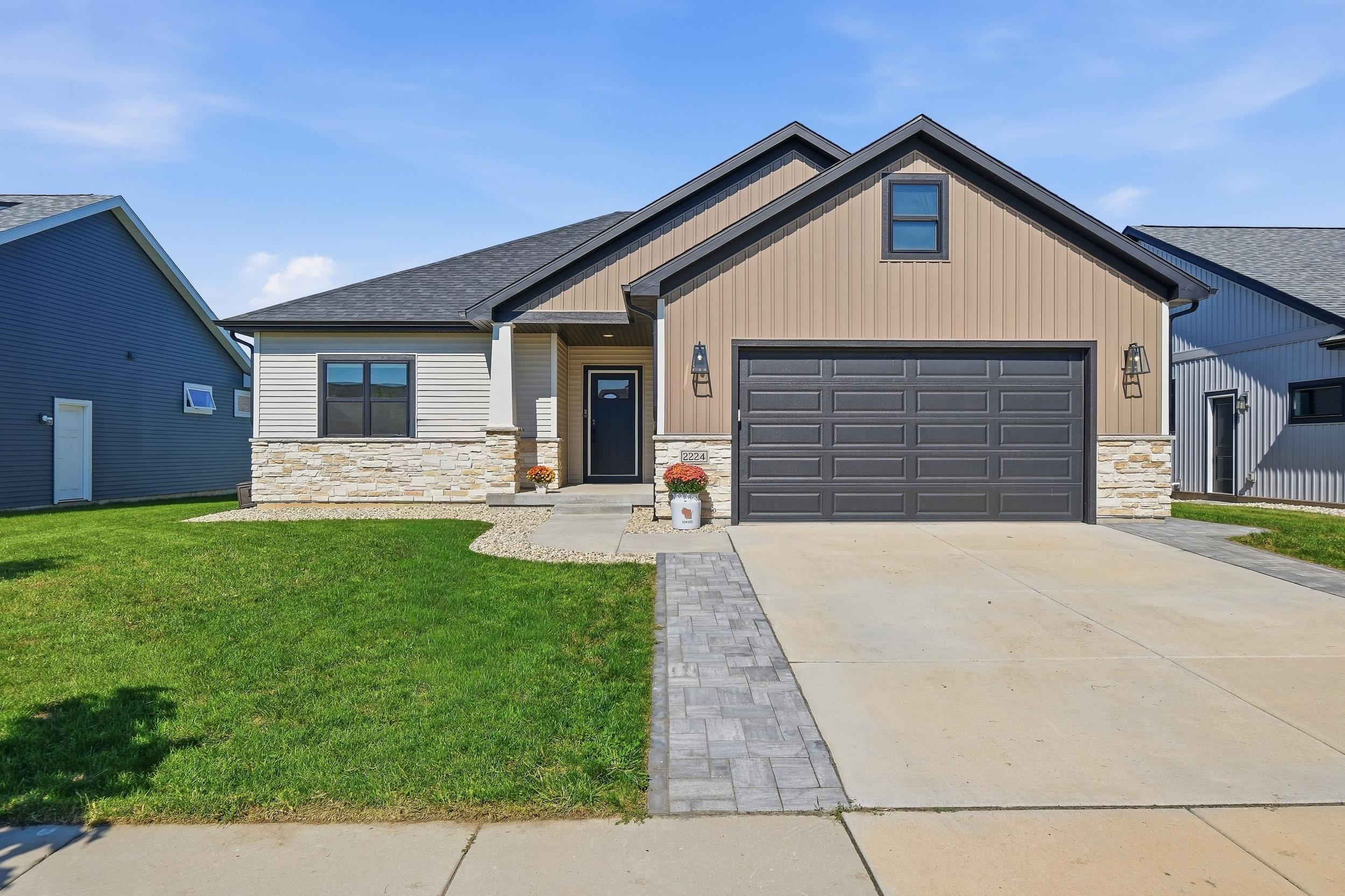 House exterior with tan siding, stone accents, and a dark double garage door.