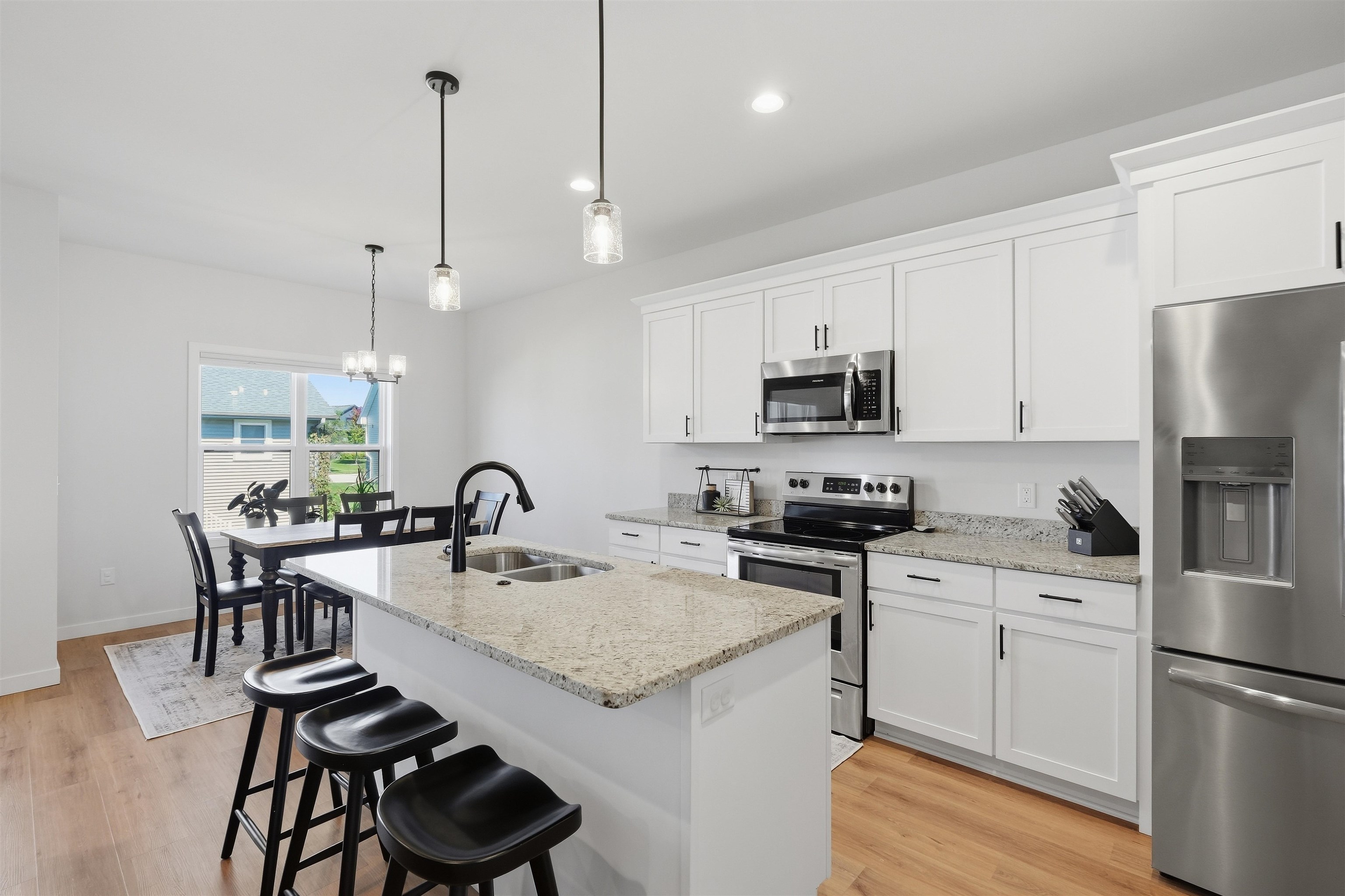 Bright kitchen with white cabinets, stainless steel appliances, and a granite island with black bar stools.