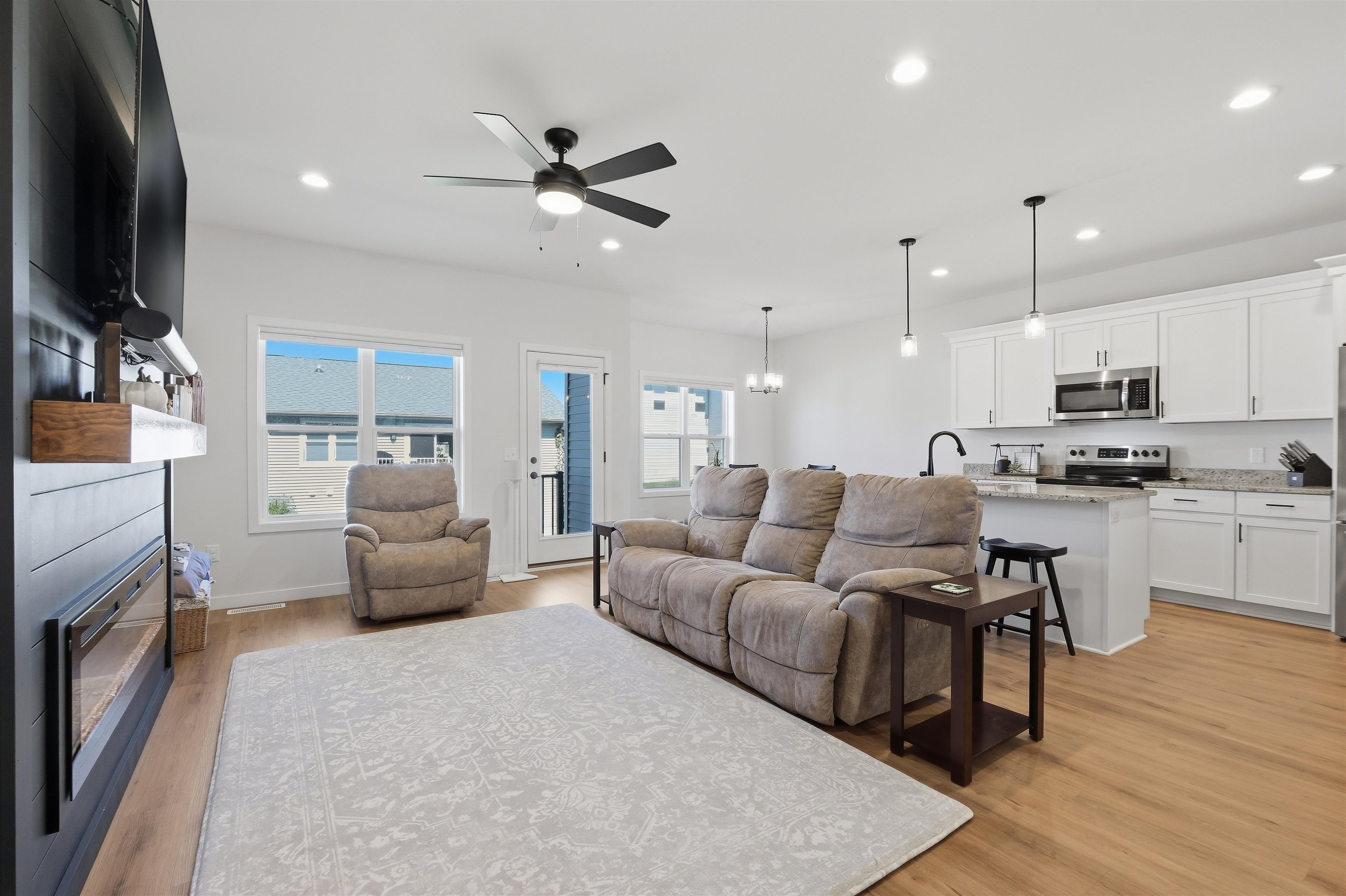Open-plan living room and kitchen with a gray sectional, recliner, pale rug, and white cabinets.