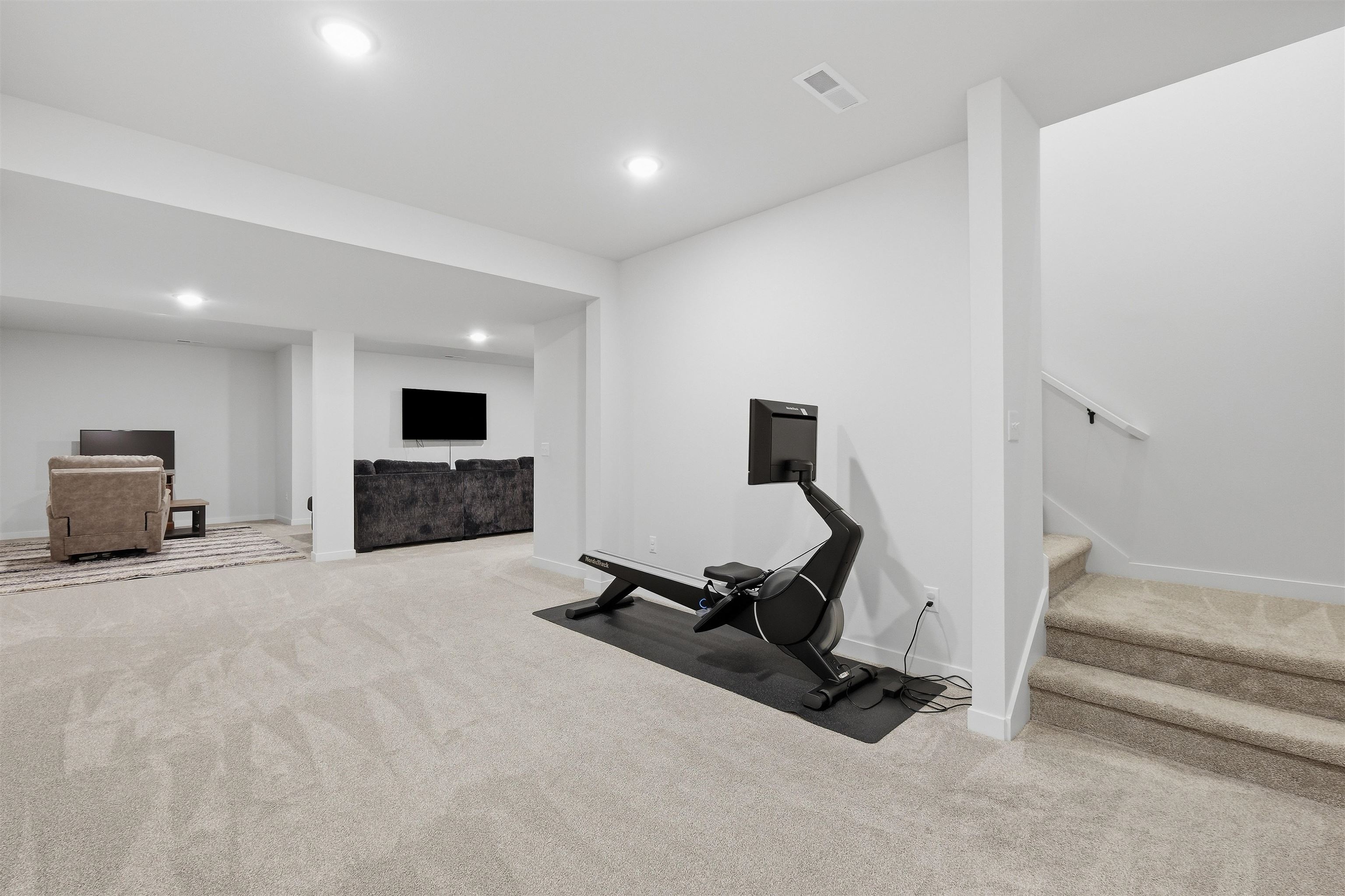 Finished basement with a rowing machine, carpeted stairs, and a TV seating area.