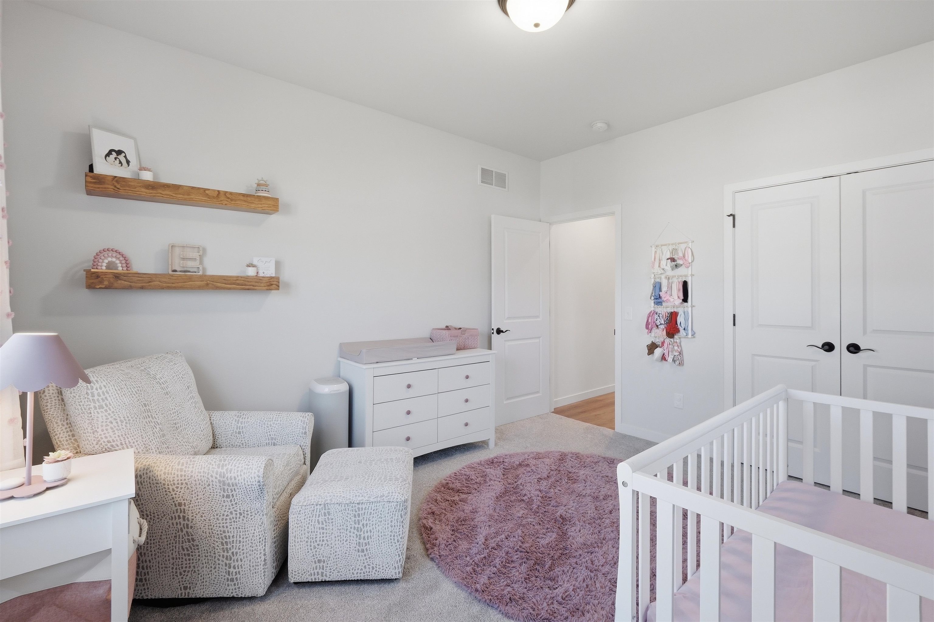 Nursery with a white crib, dresser and changing pad, patterned glider, and mauve rug.