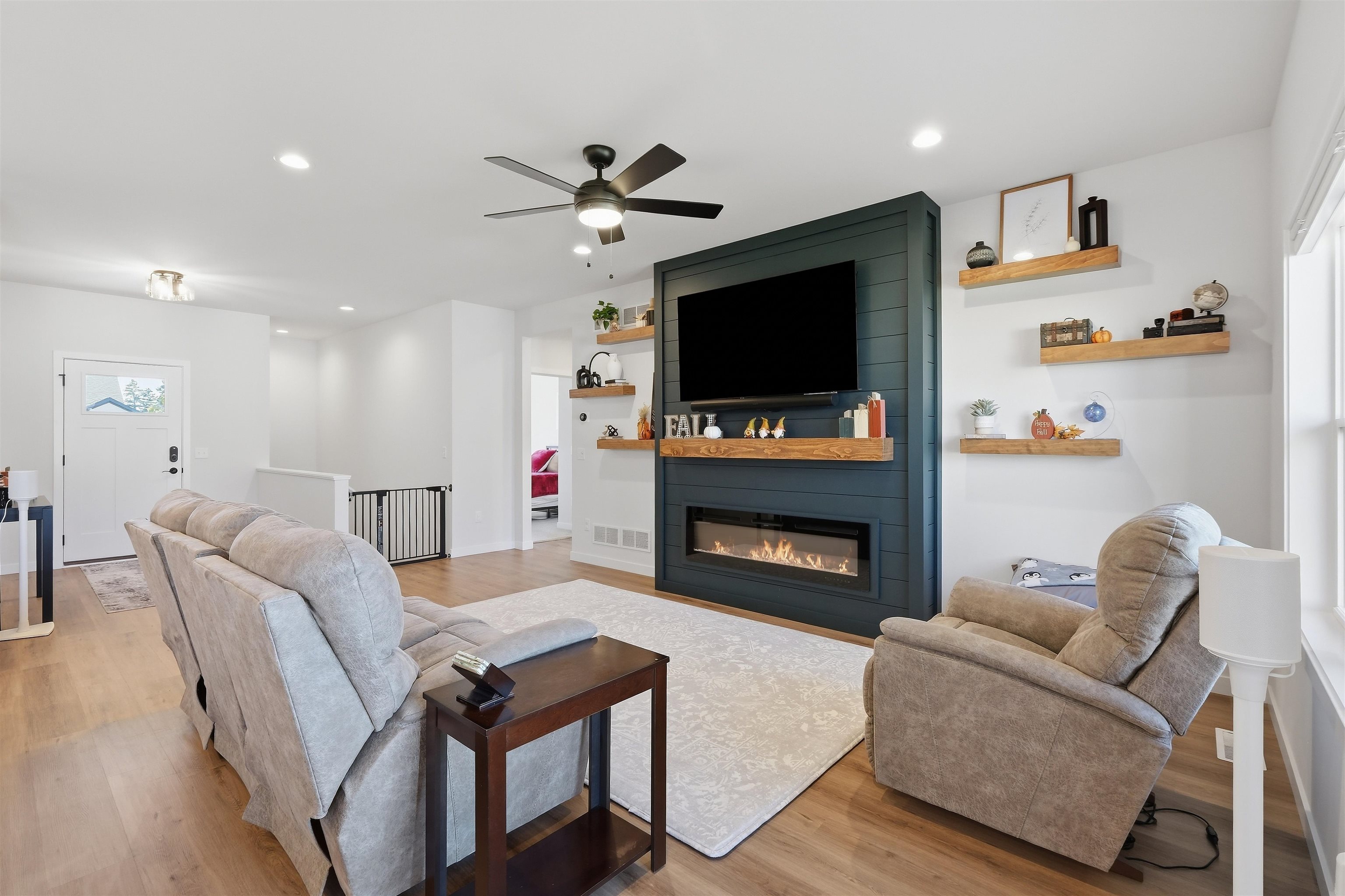 Living room with a dark teal fireplace wall, floating shelves, and gray seating.