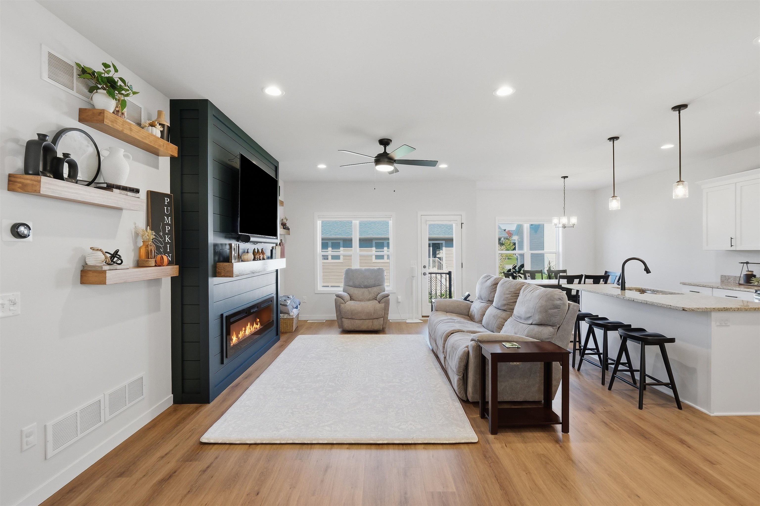 Open-plan living room with gray seating, a dark built-in fireplace wall, and kitchen island.