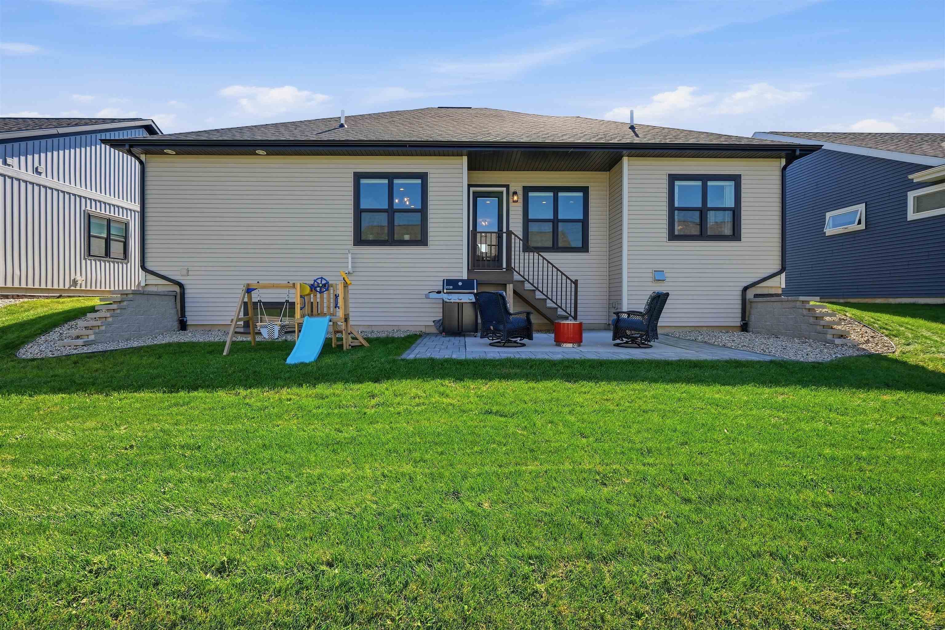 Rear of a light-sided home with a patio, outdoor seating, children’s playset, and broad lawn.