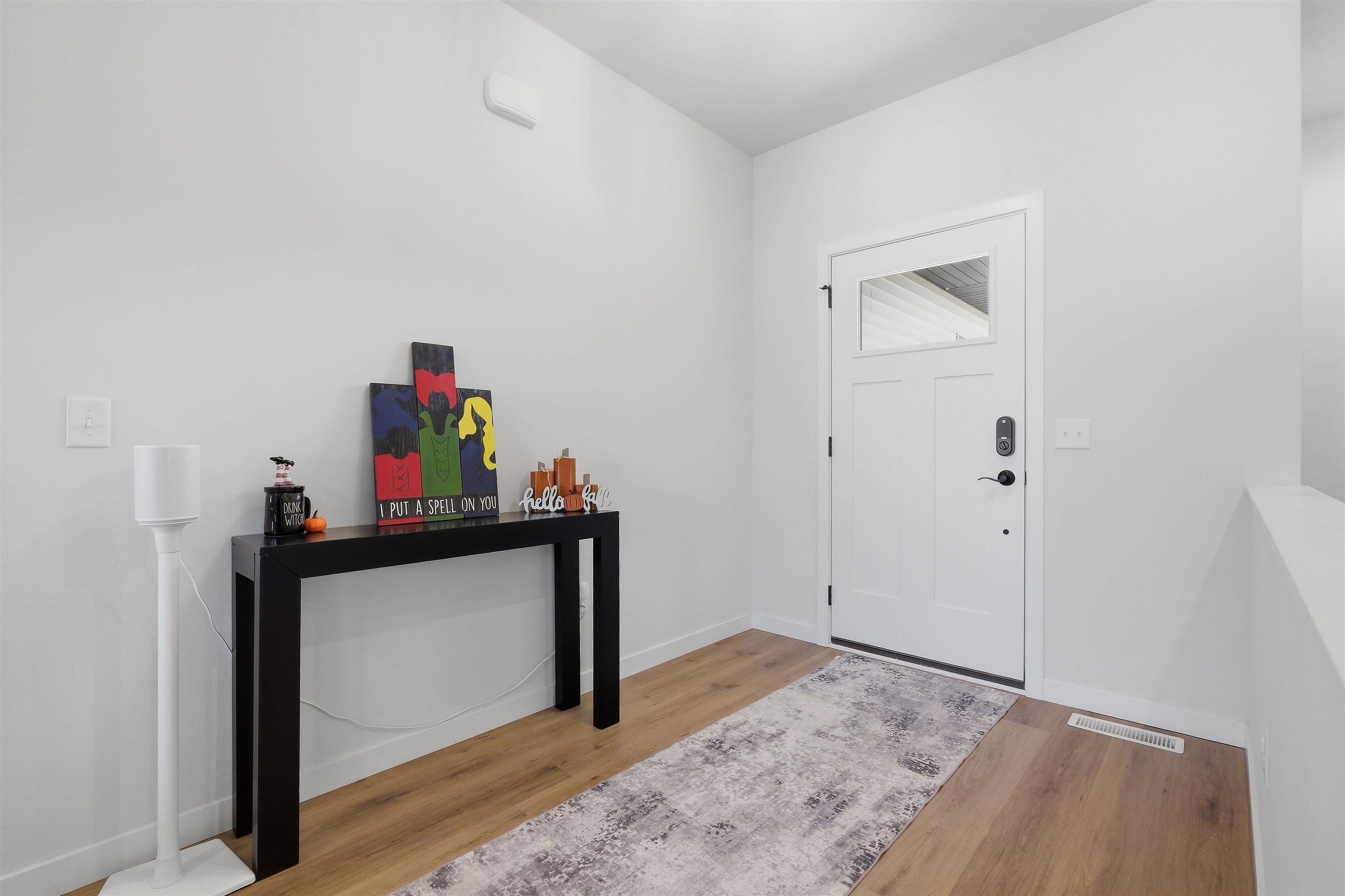 Entryway with a white front door, patterned runner, and black console table with seasonal decor.