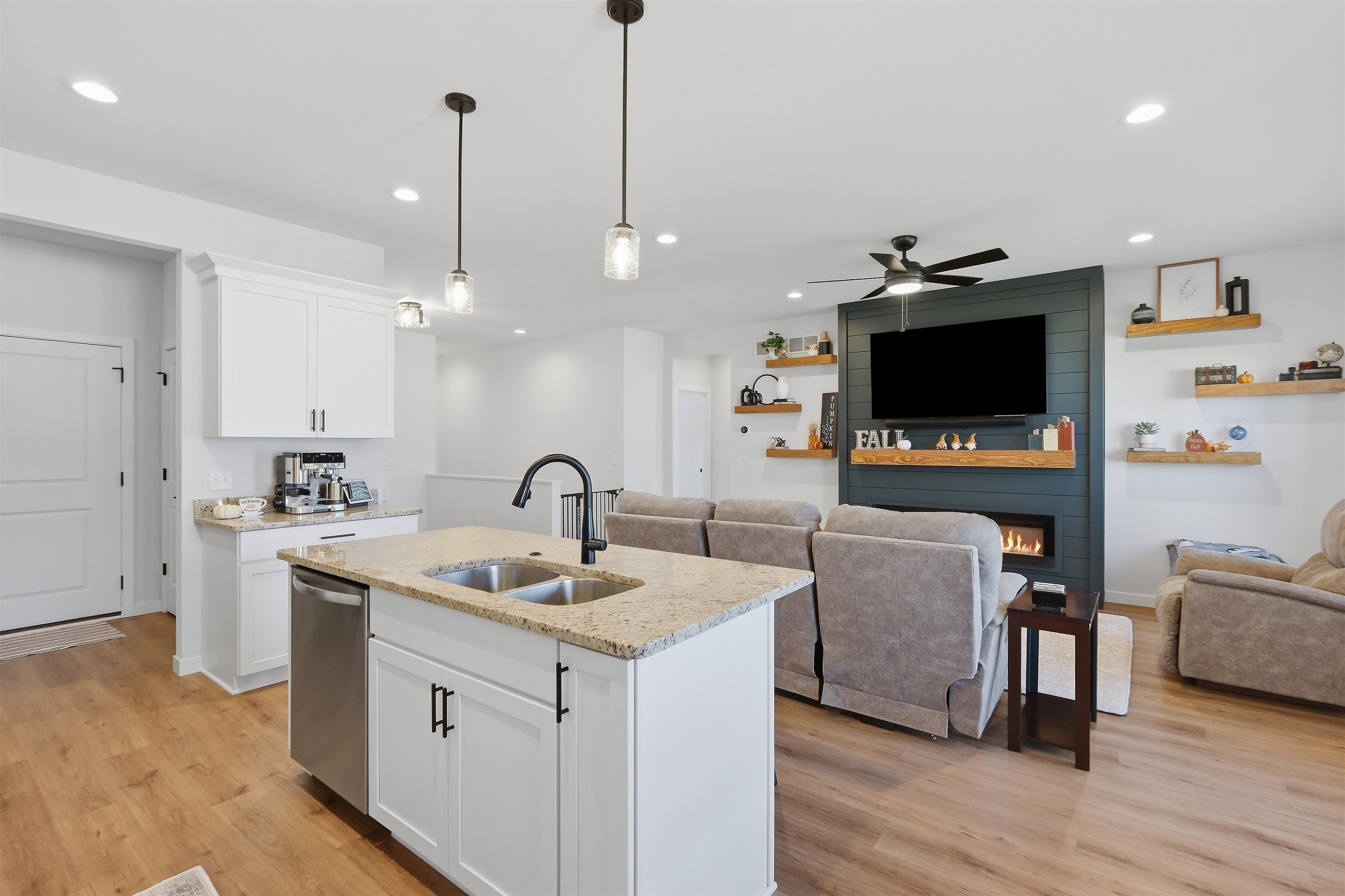 Open-plan kitchen with a granite island and sink facing a furnished living room with a dark fireplace wall.