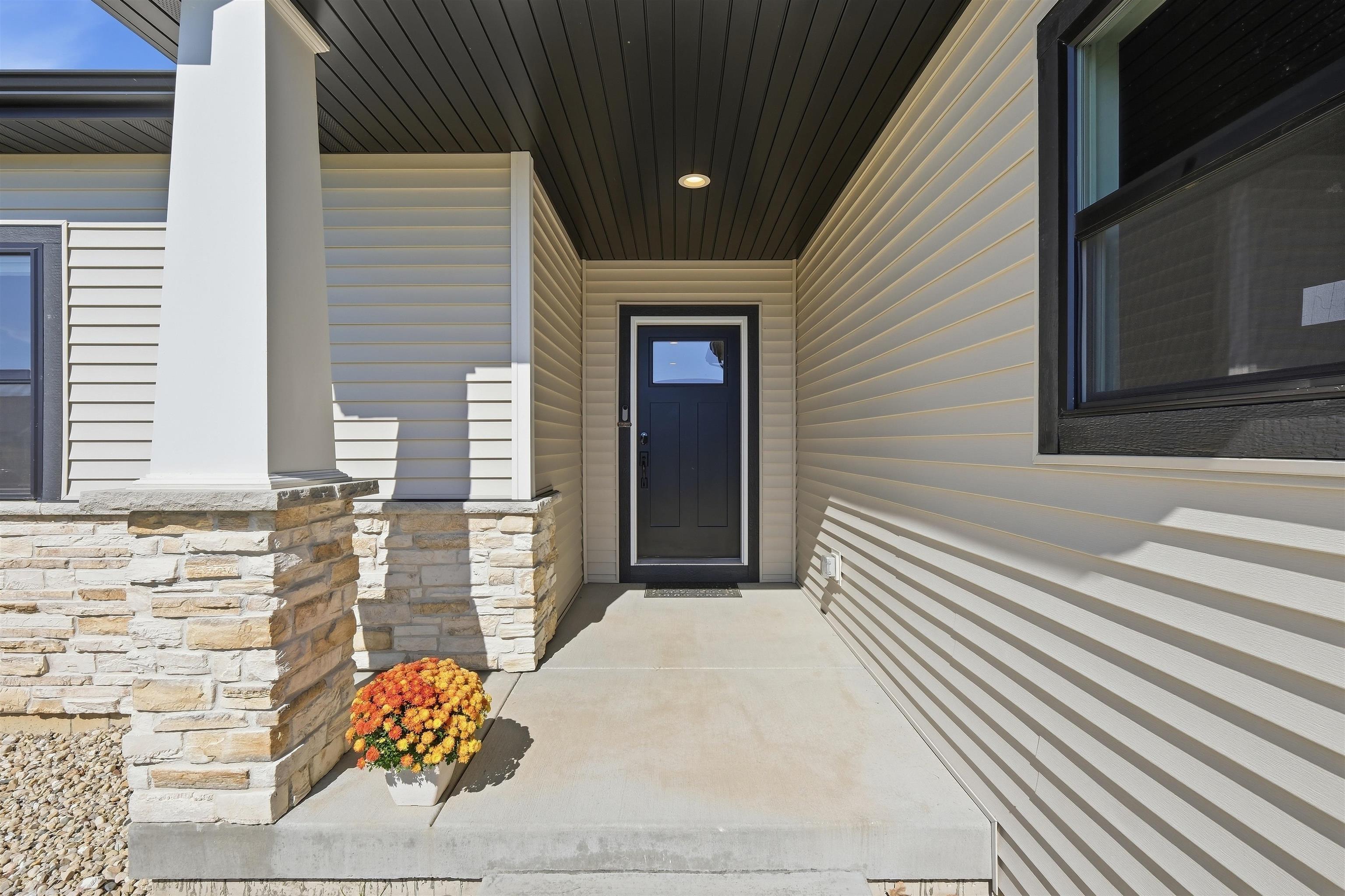 Covered front porch with a dark entry door, stone column, and potted flowers.