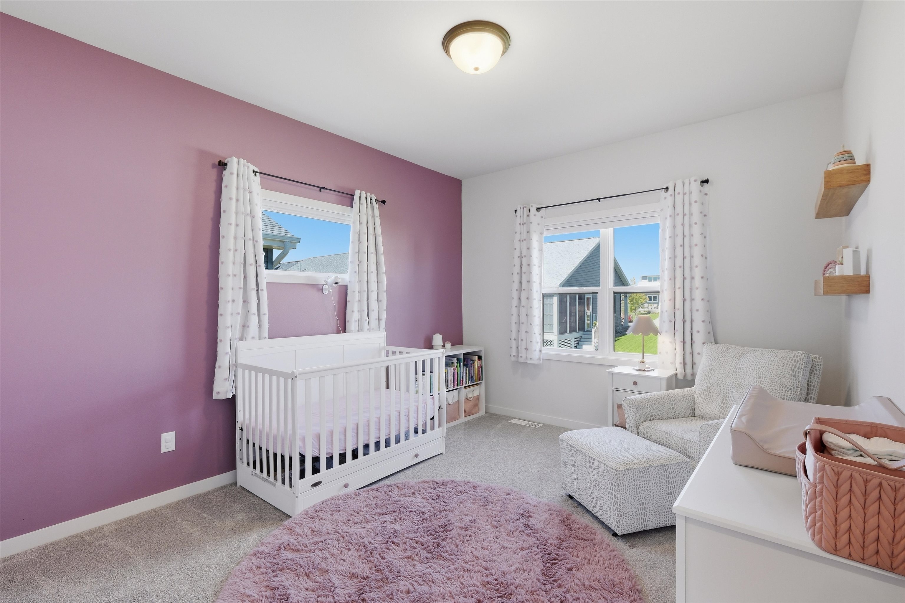 Nursery with a white crib, mauve accent wall, and patterned glider.
