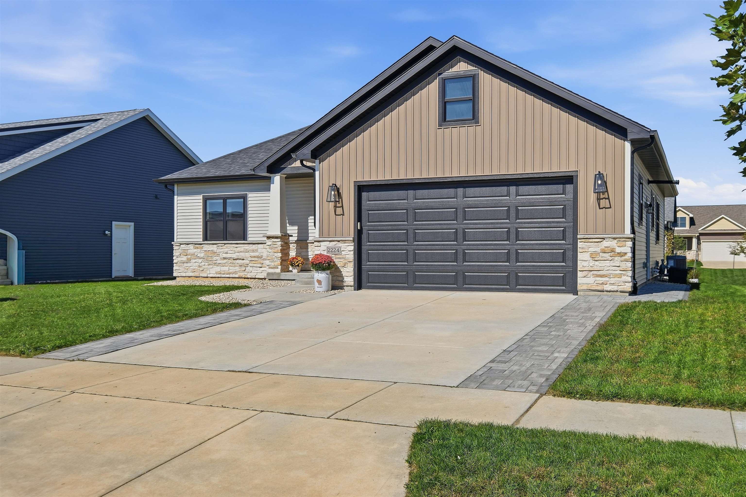 Tan-sided home with stone veneer and a large dark garage door beside a wide driveway.