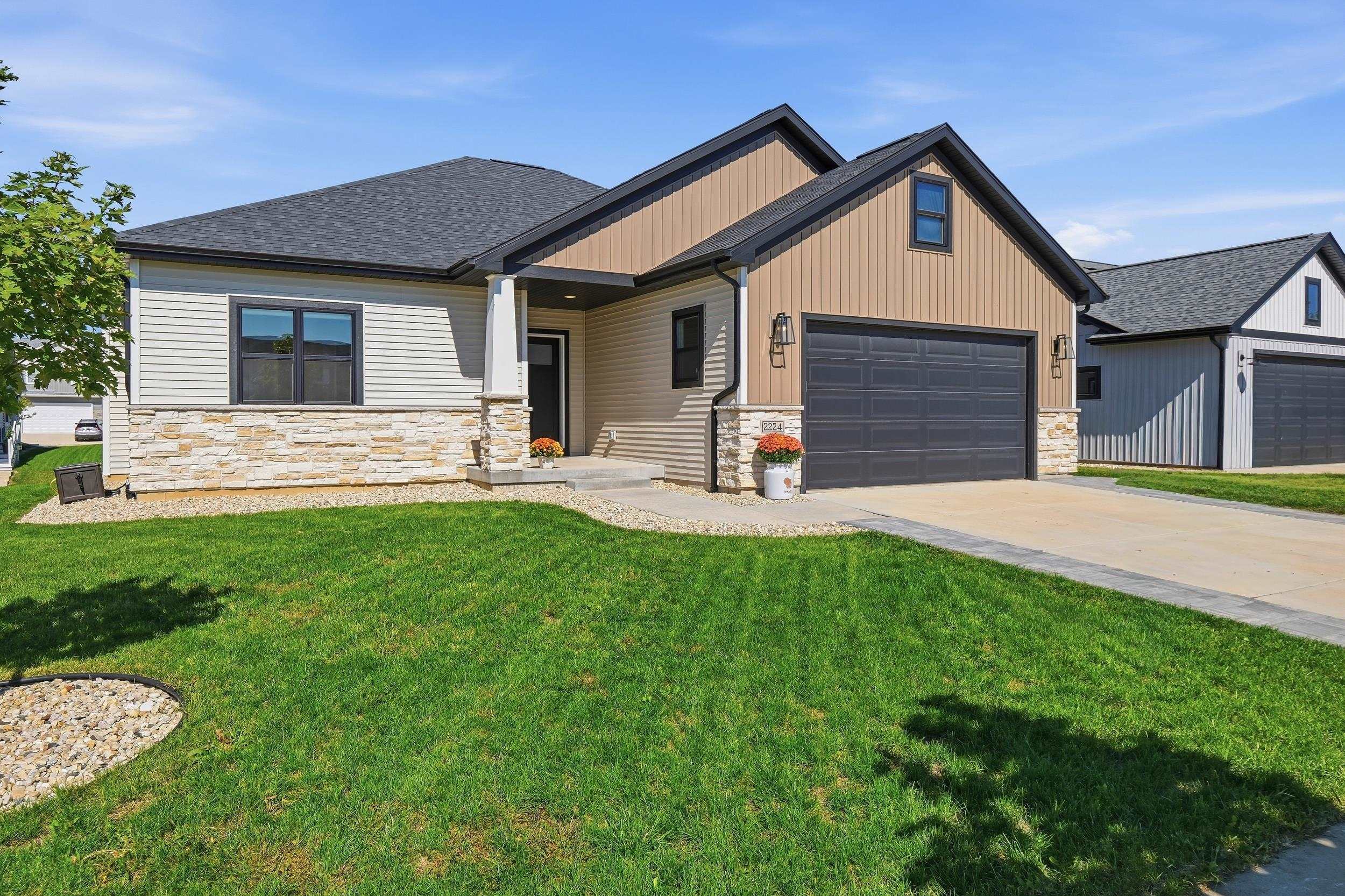 House with tan siding, stone veneer, a dark double garage, and a broad front lawn.