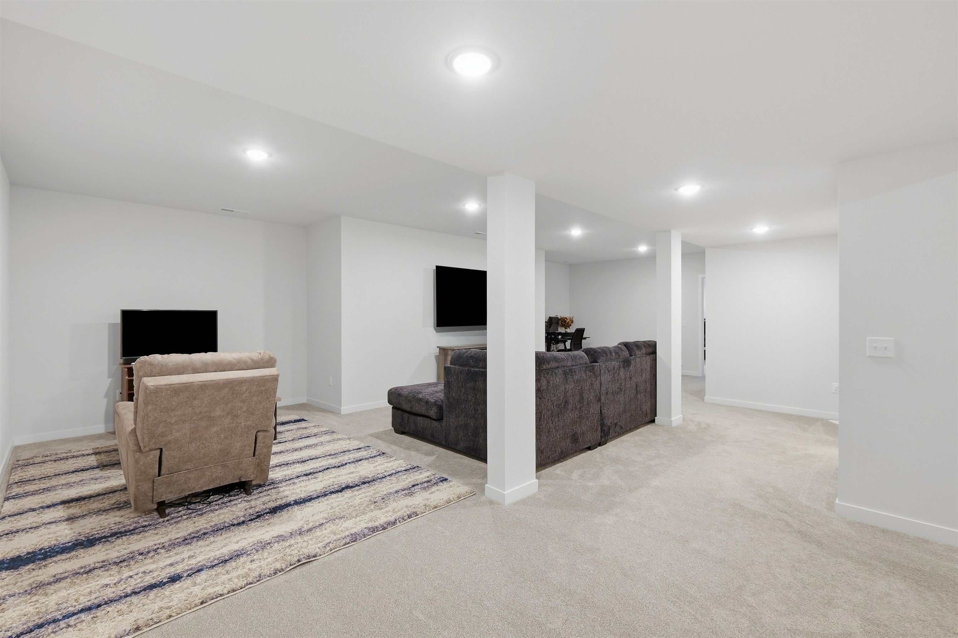 Furnished basement living room with a sectional sofa, armchair, and striped area rug.