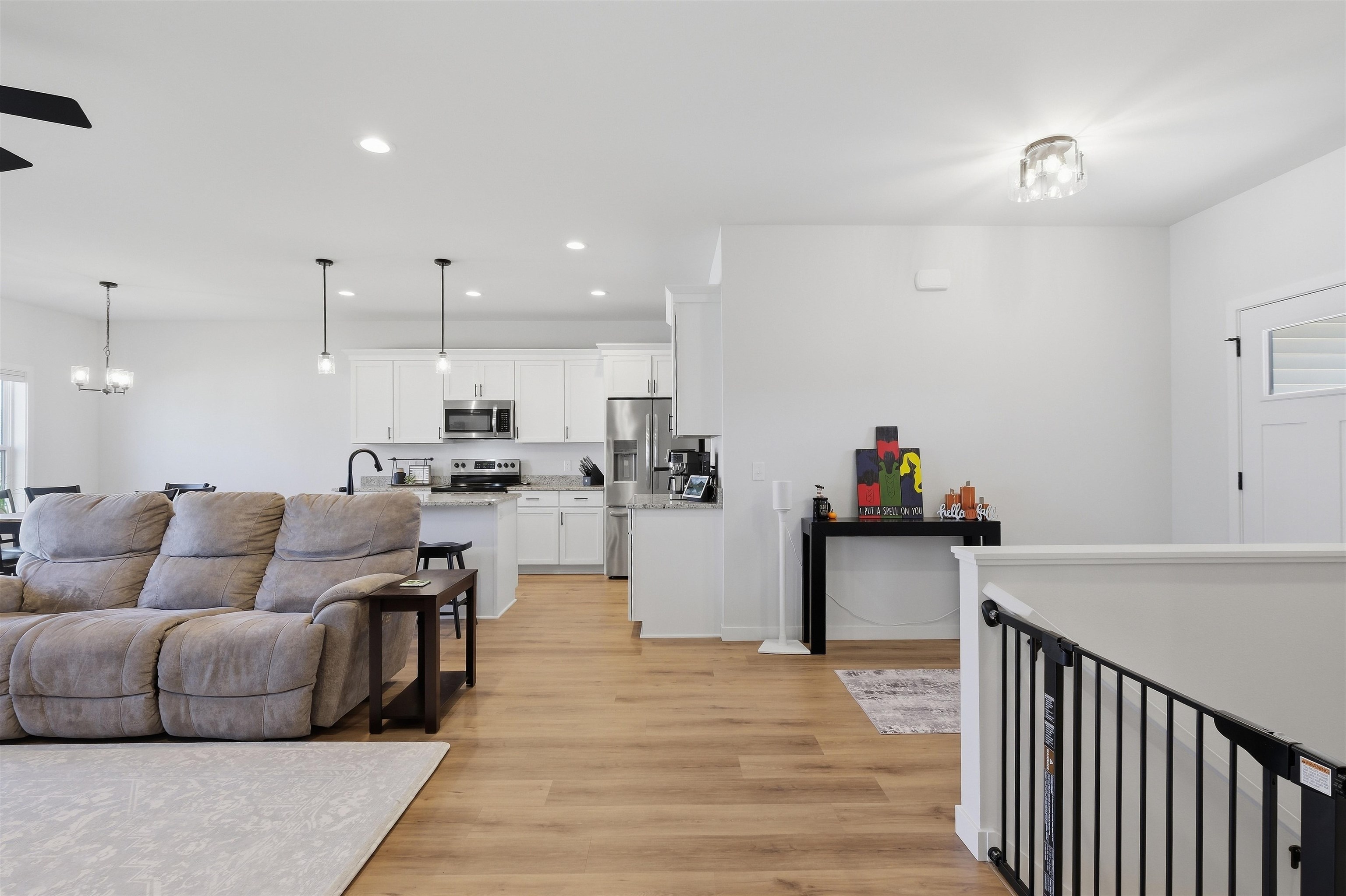 Open-plan living room and kitchen with white cabinets, stainless appliances, and a gray reclining sofa.