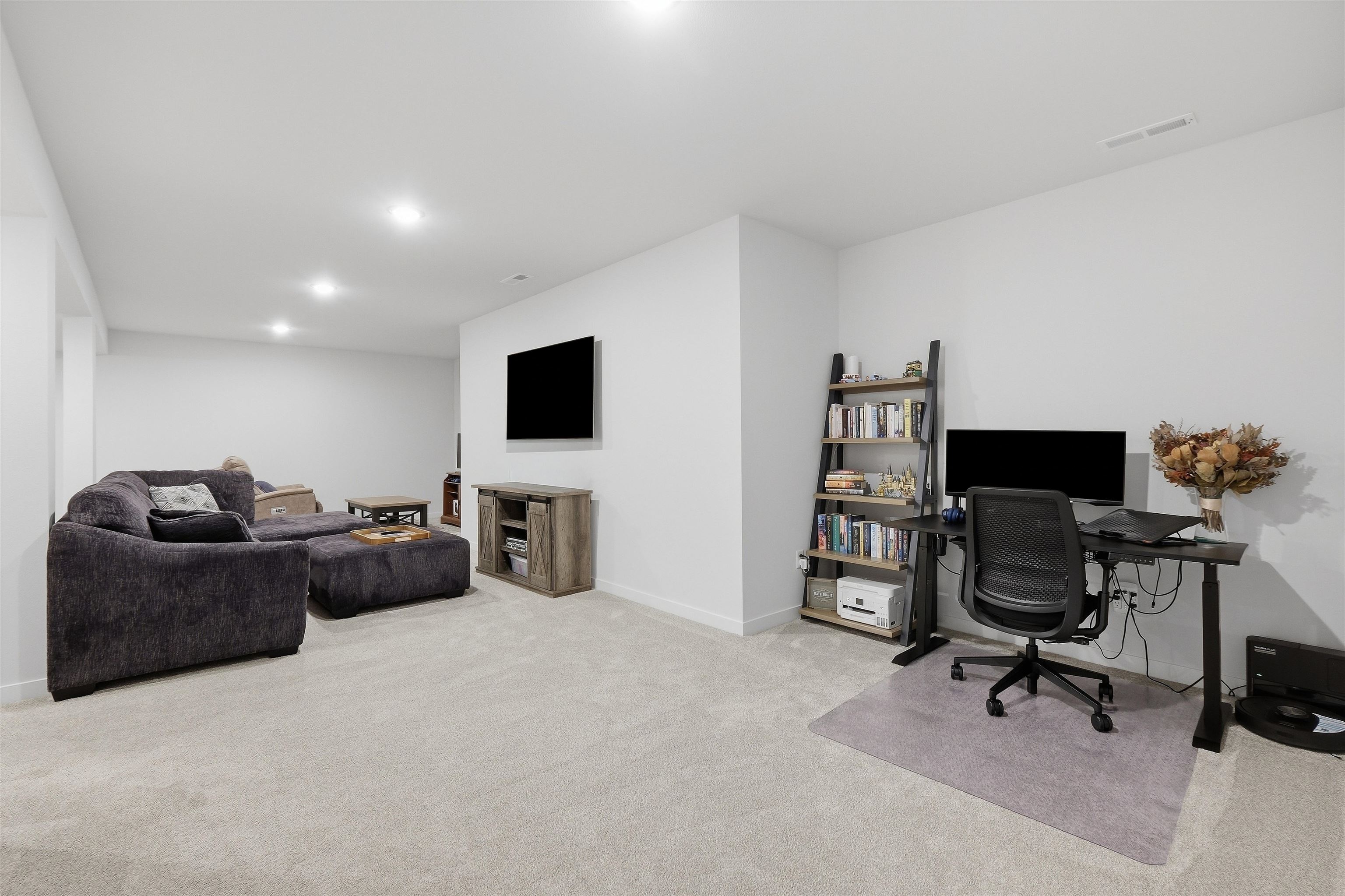 Furnished basement living area with a sectional sofa, wall-mounted TV, and adjacent home office.