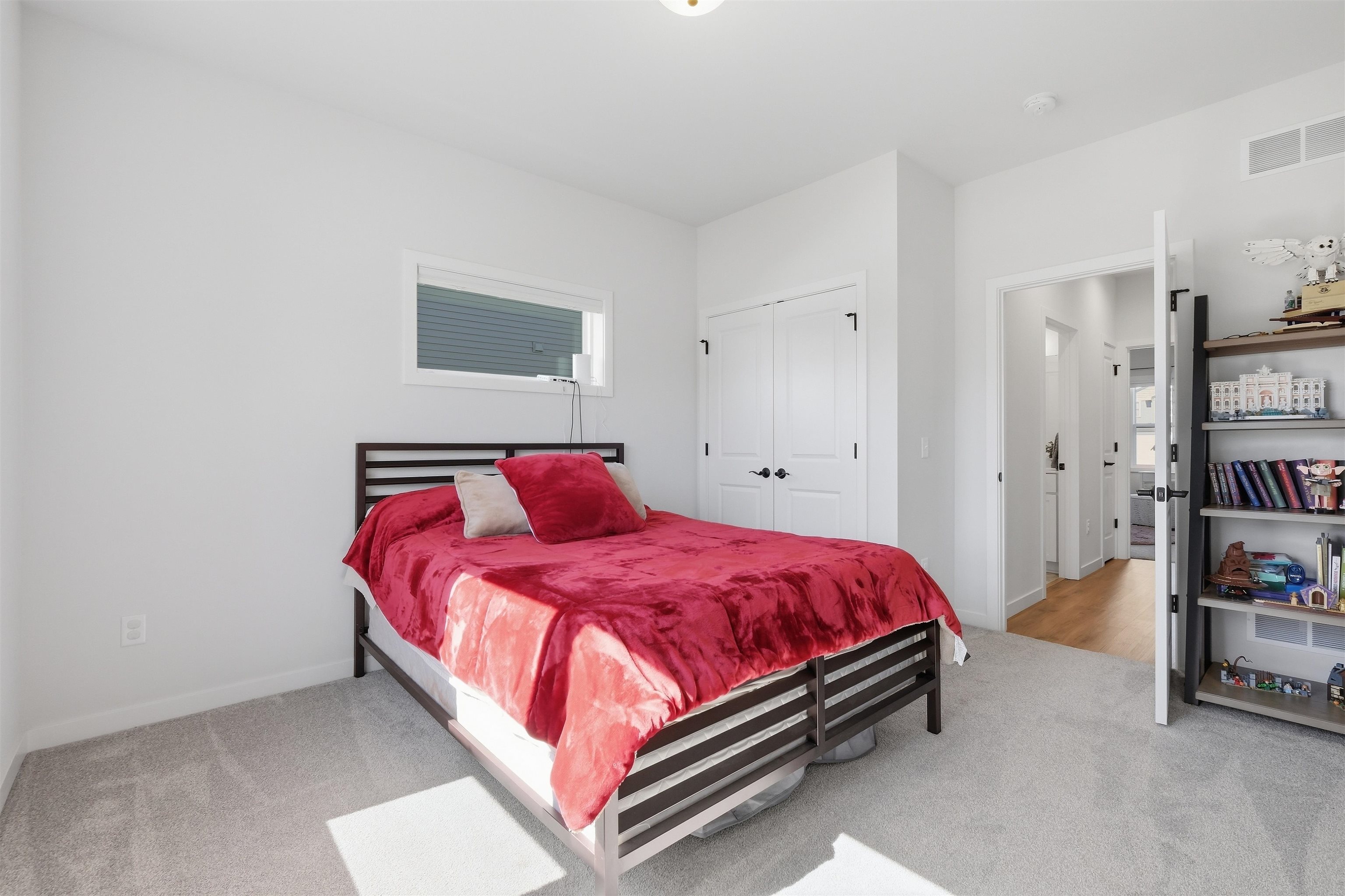 Furnished bedroom with vivid red bedding, a dark slatted bed frame, and a tall shelving unit.