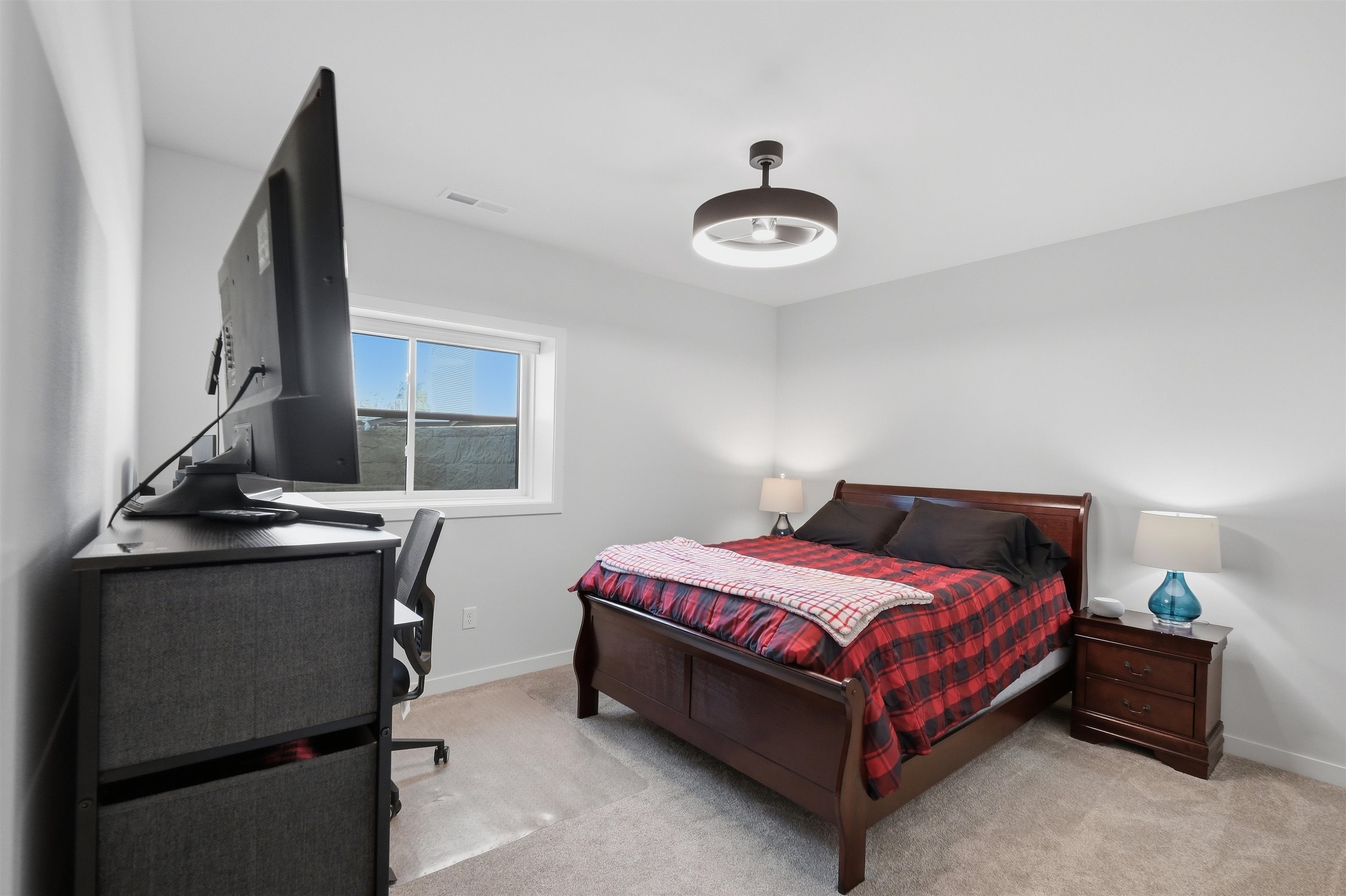 Bedroom with a dark wood bed, red plaid bedding, and a desk beside the window.