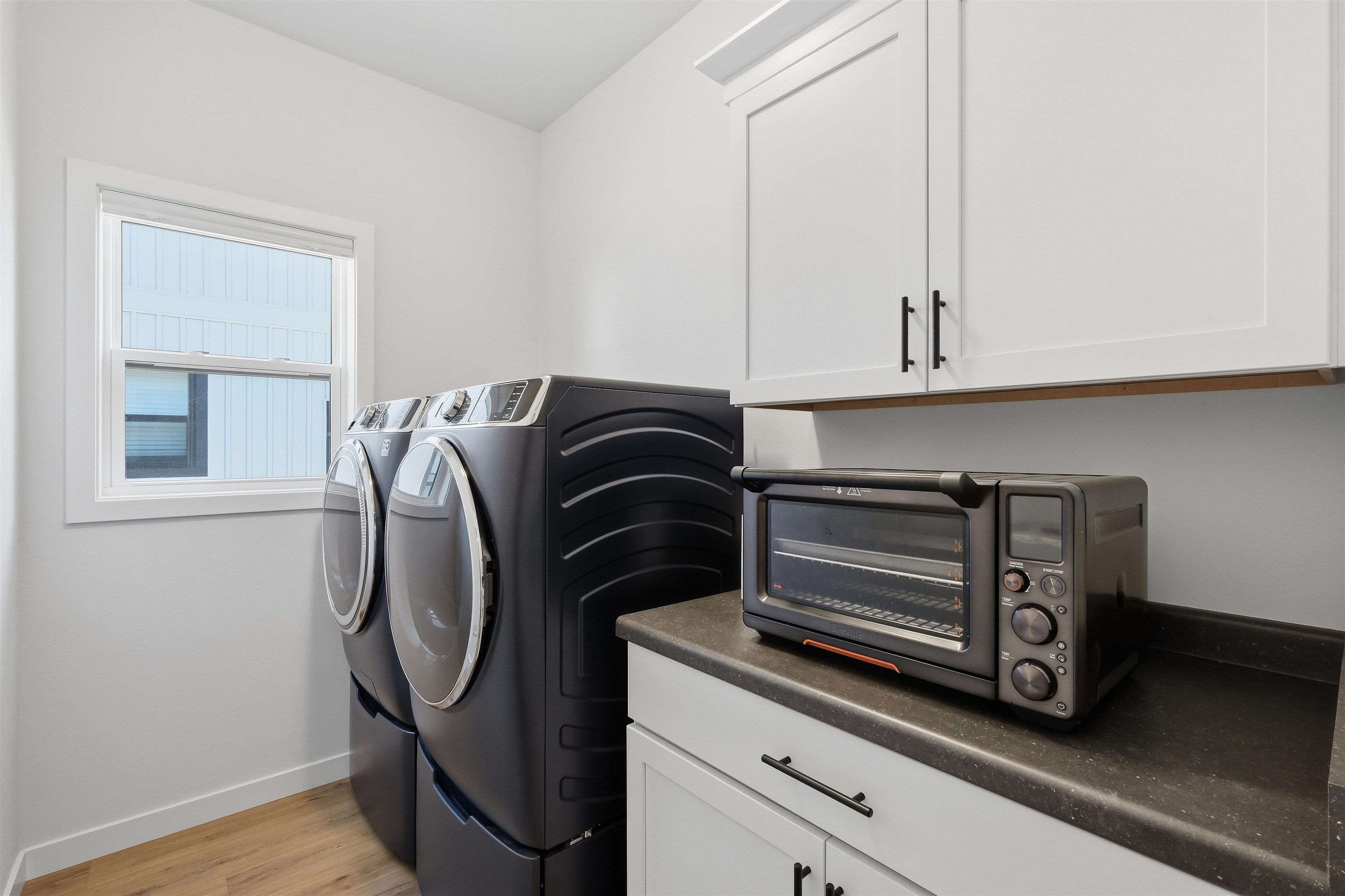 Laundry room with front-loading washer and dryer, white cabinets, and a countertop toaster oven.