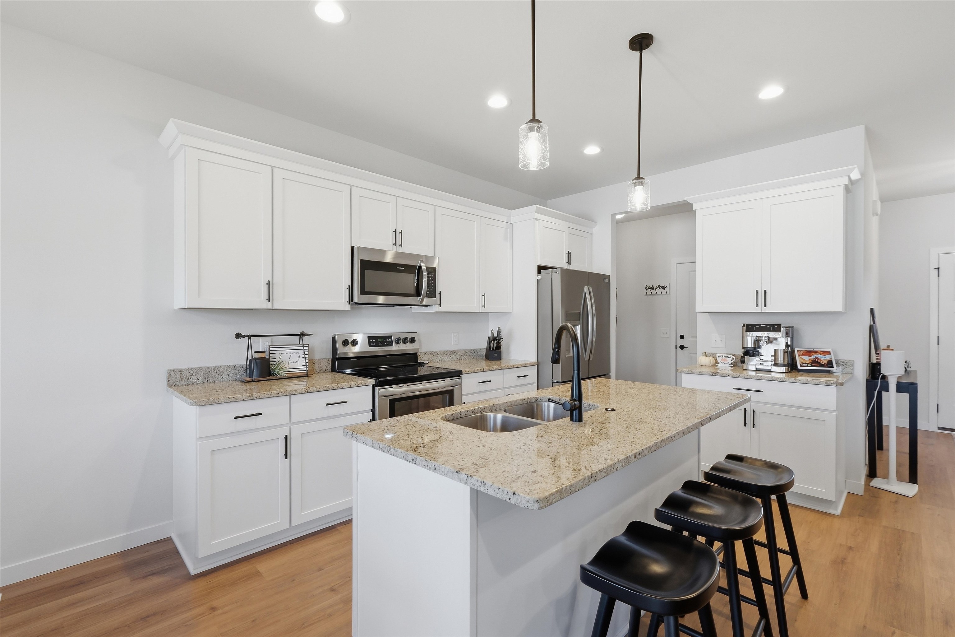 Modern white kitchen with a stone-topped island, stainless steel appliances, and black bar stools