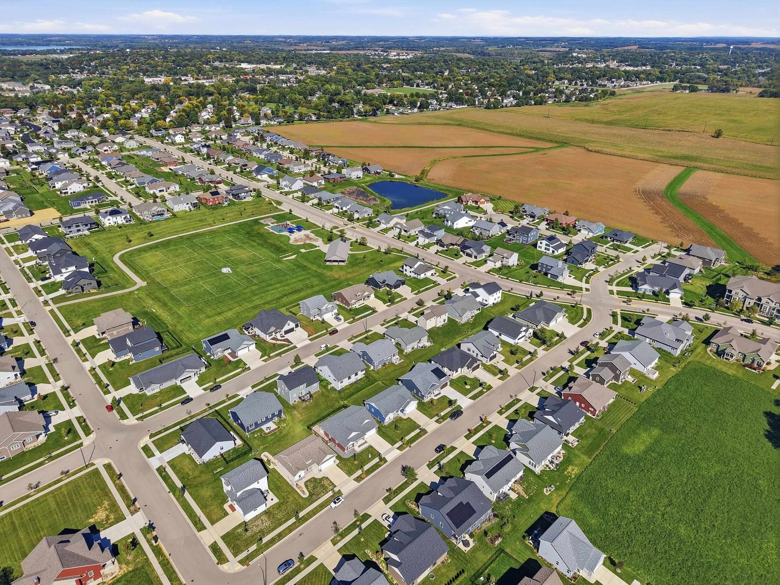 Aerial view of a residential neighborhood beside a soccer field, pond, and open farmland.