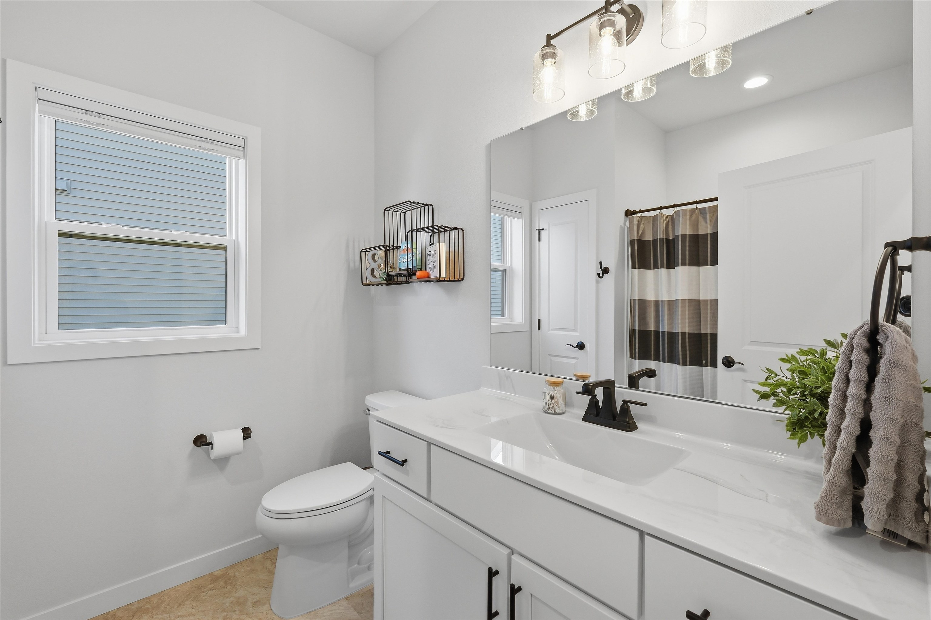Bright bathroom with a white vanity, black fixtures, large mirror, and striped shower curtain.