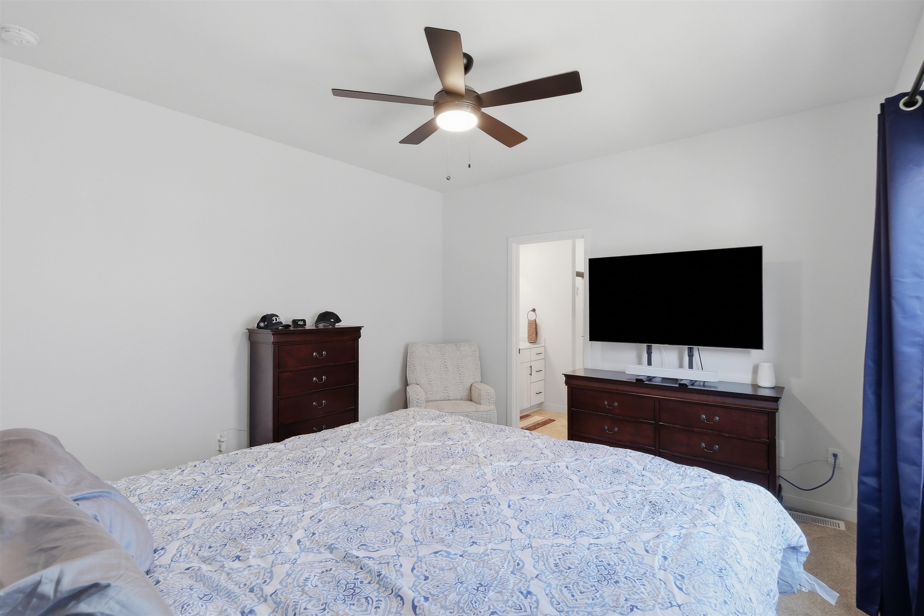 Bedroom with blue-and-white patterned bedding, dark wood dressers, and a wall-mounted television.