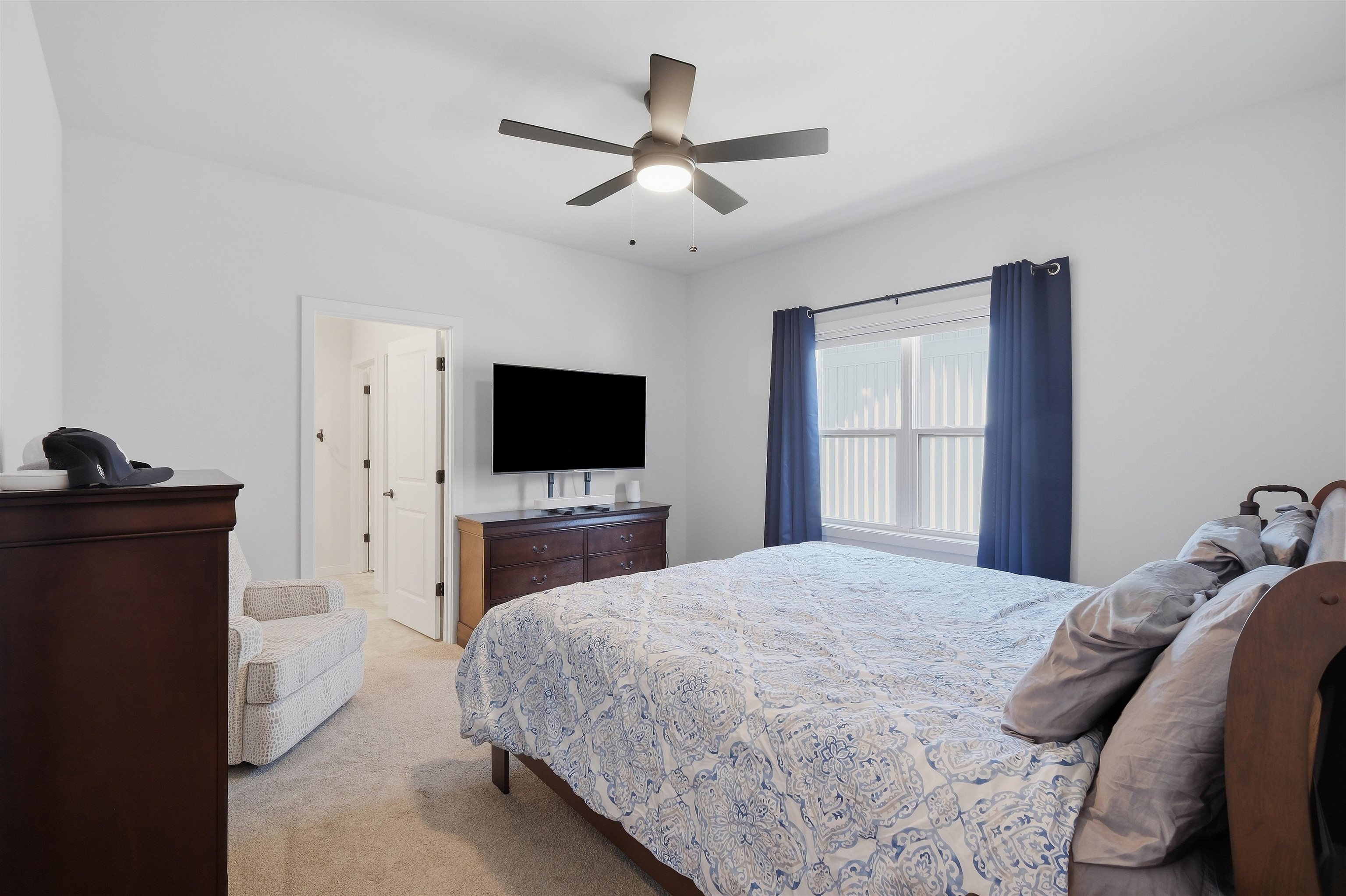 Bedroom with blue-and-white patterned bedding, navy curtains, and a ceiling fan.