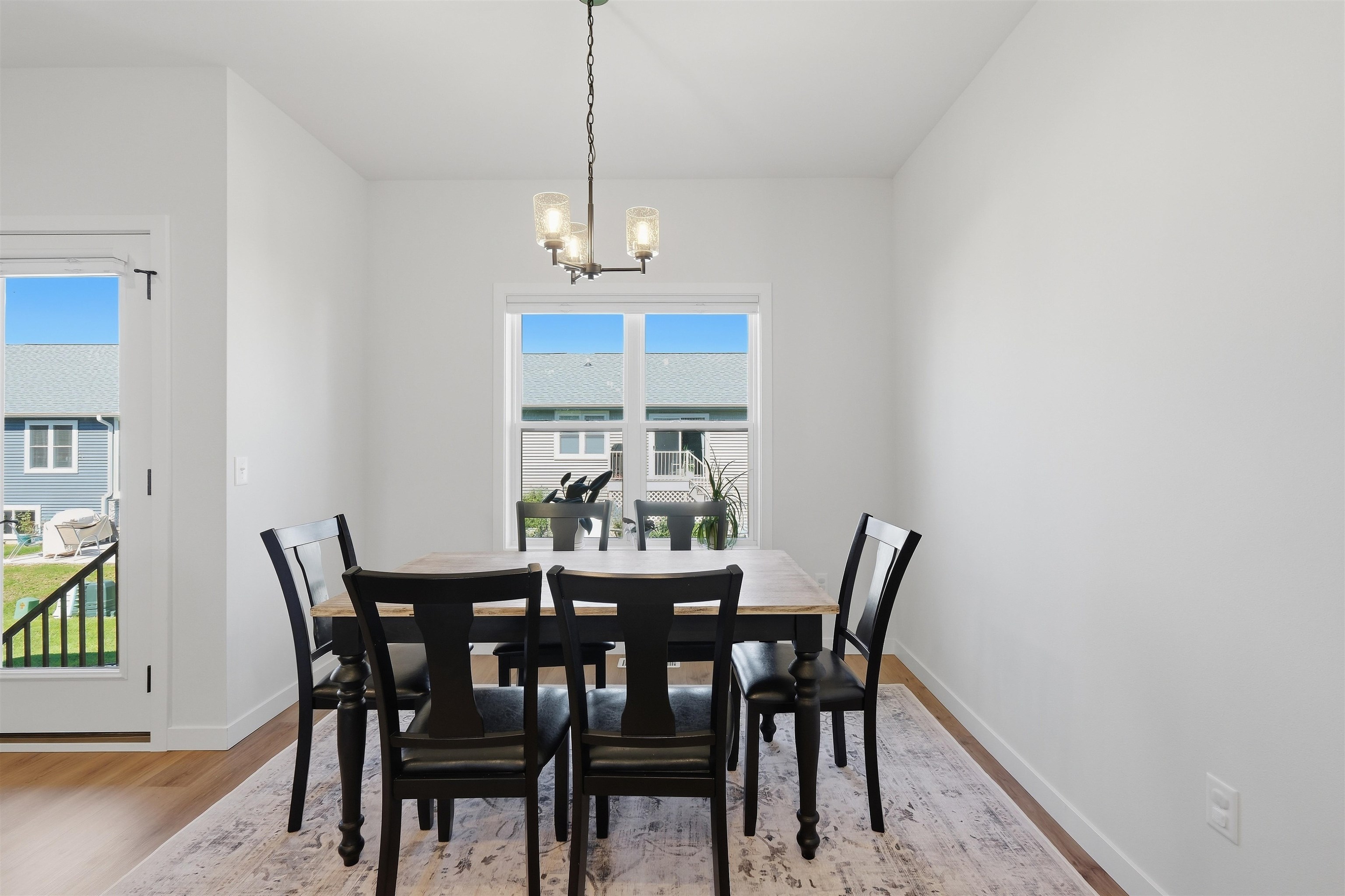 Dining room with a wood table, black chairs, patterned rug, and three-light chandelier.