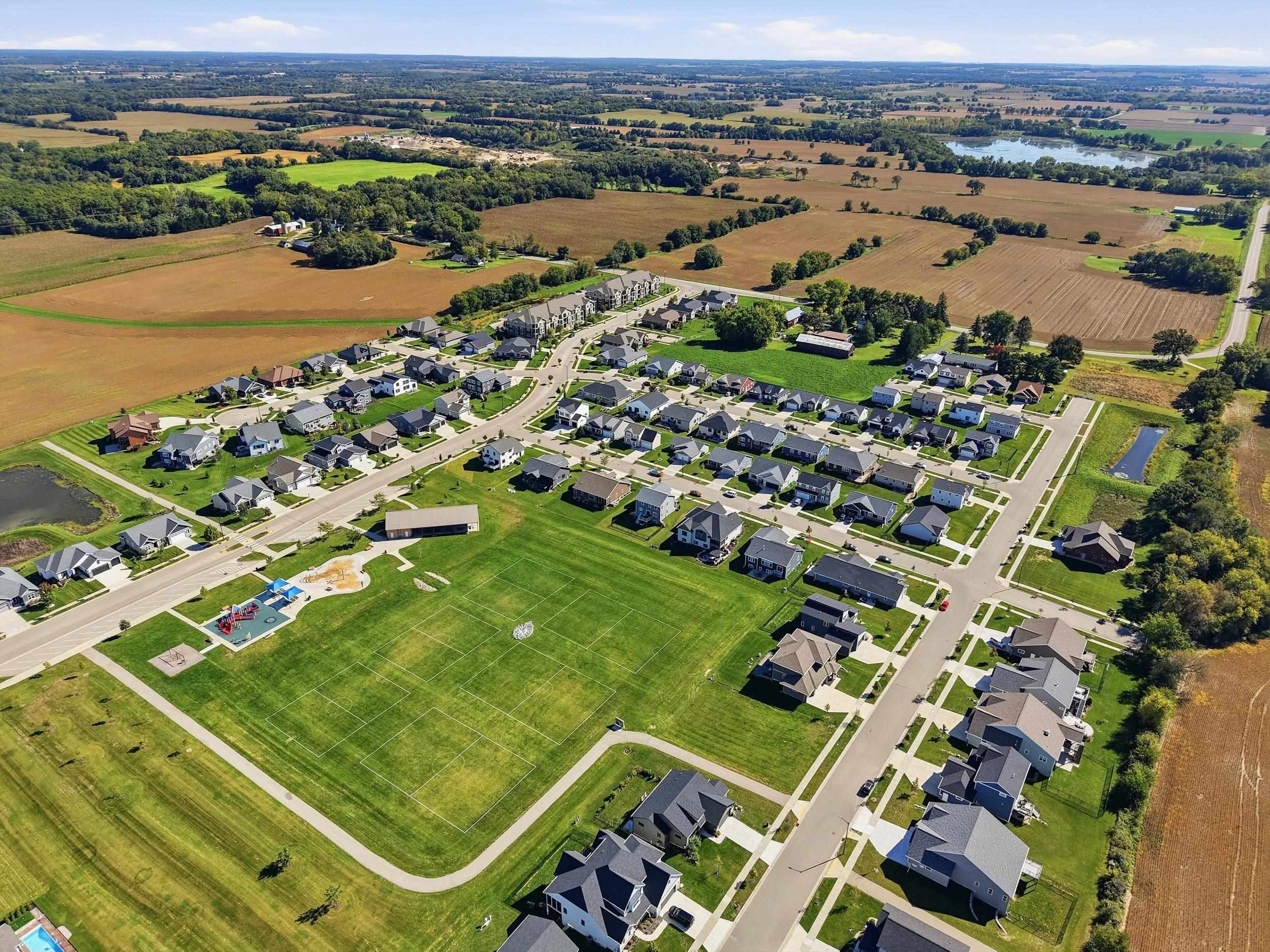 Aerial view of a subdivision with a large recreation field, playground, and surrounding farmland.