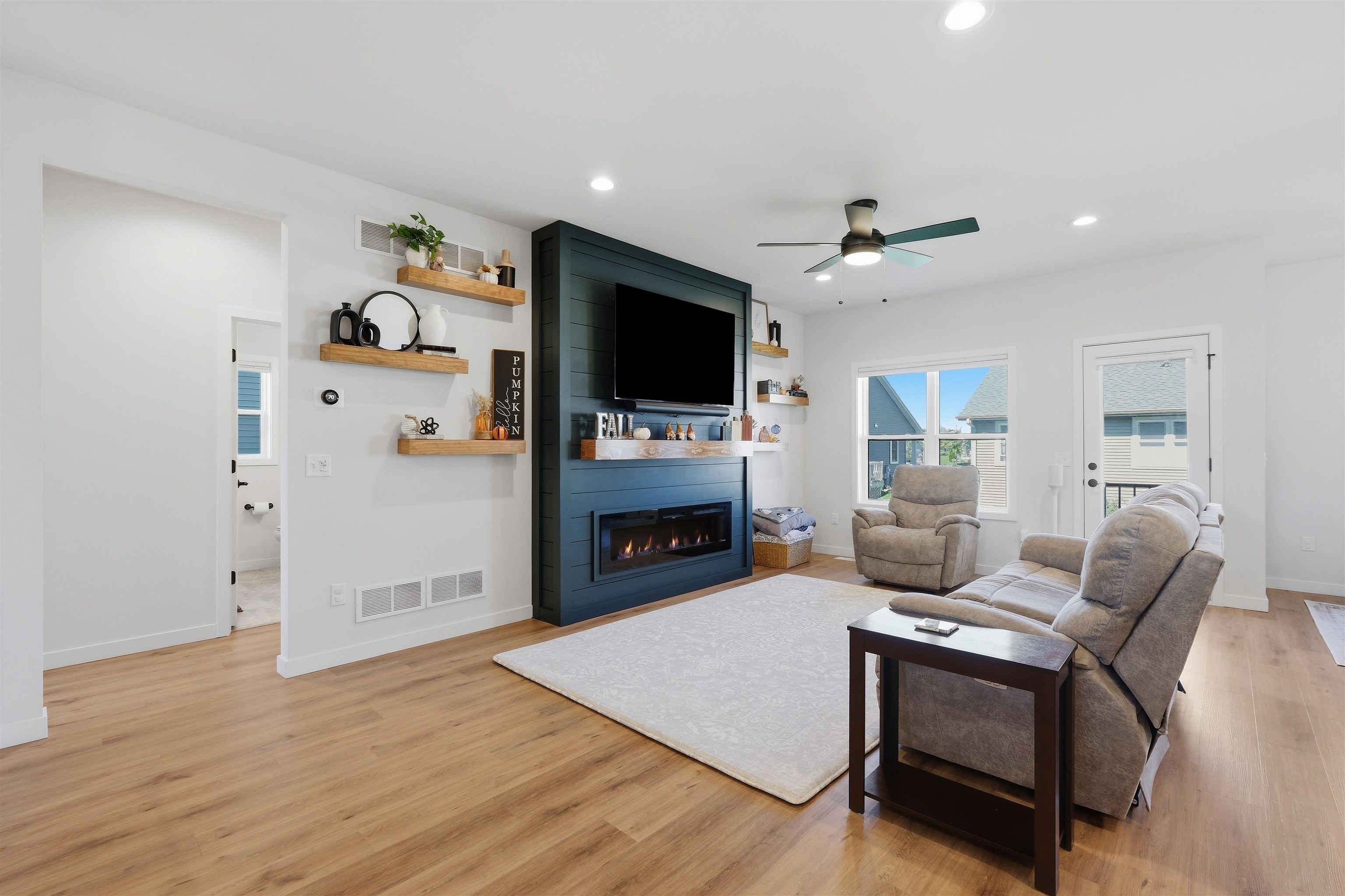 Living room with a dark blue fireplace wall, floating wood shelves, and gray seating.