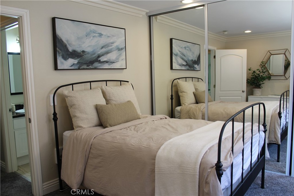 Staged bedroom with a black metal bed, neutral bedding, and mirrored closet doors.