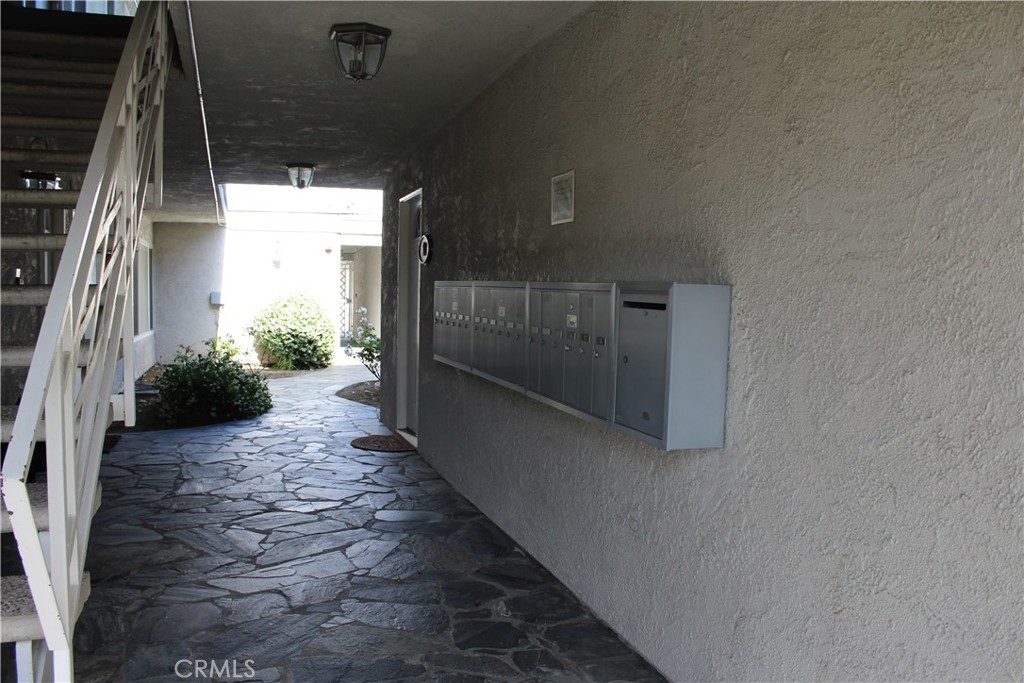 Covered apartment walkway with stone flooring, a staircase, and a row of mailboxes.