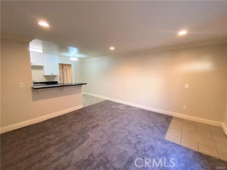 Vacant living area with gray carpet and a kitchen pass-through.