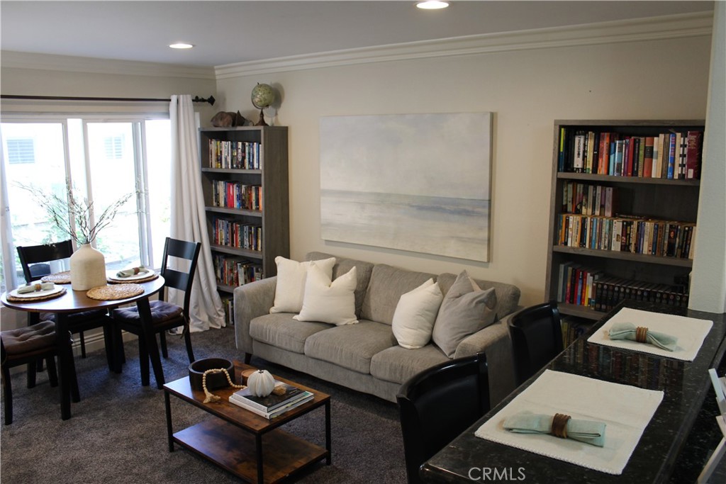 Living and dining area with a gray sofa, tall bookcases, and large windows.