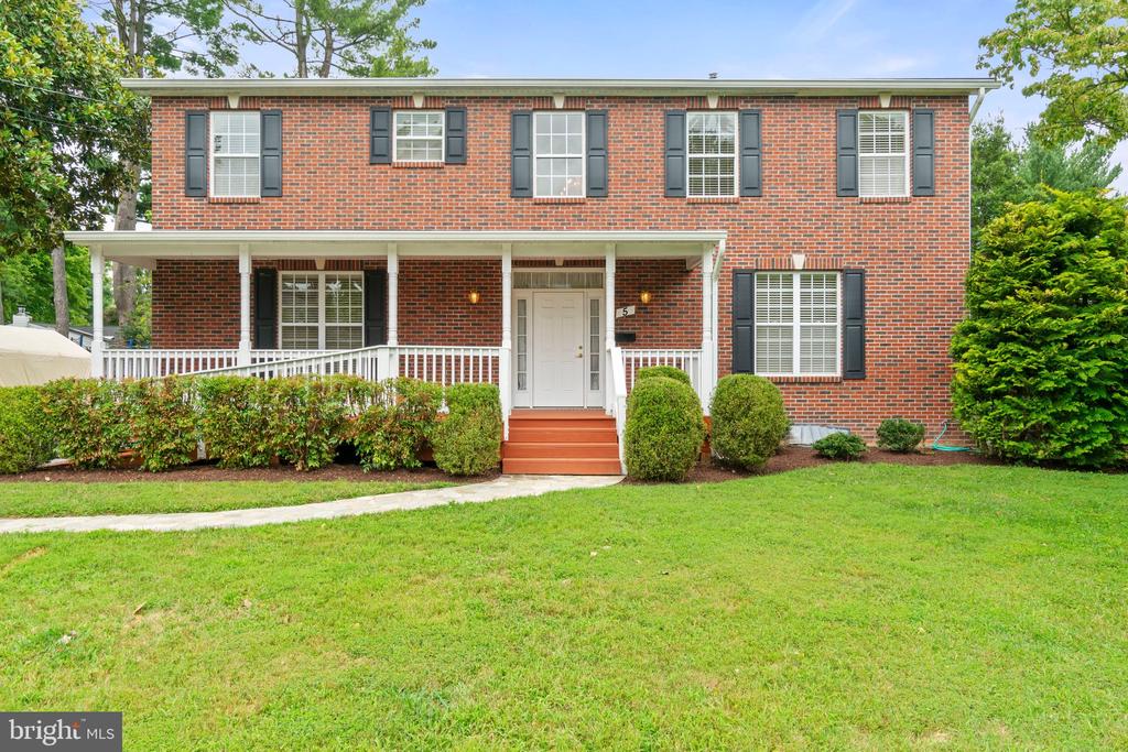 Two-story red brick house with dark shutters and a covered front porch overlooking a broad lawn.