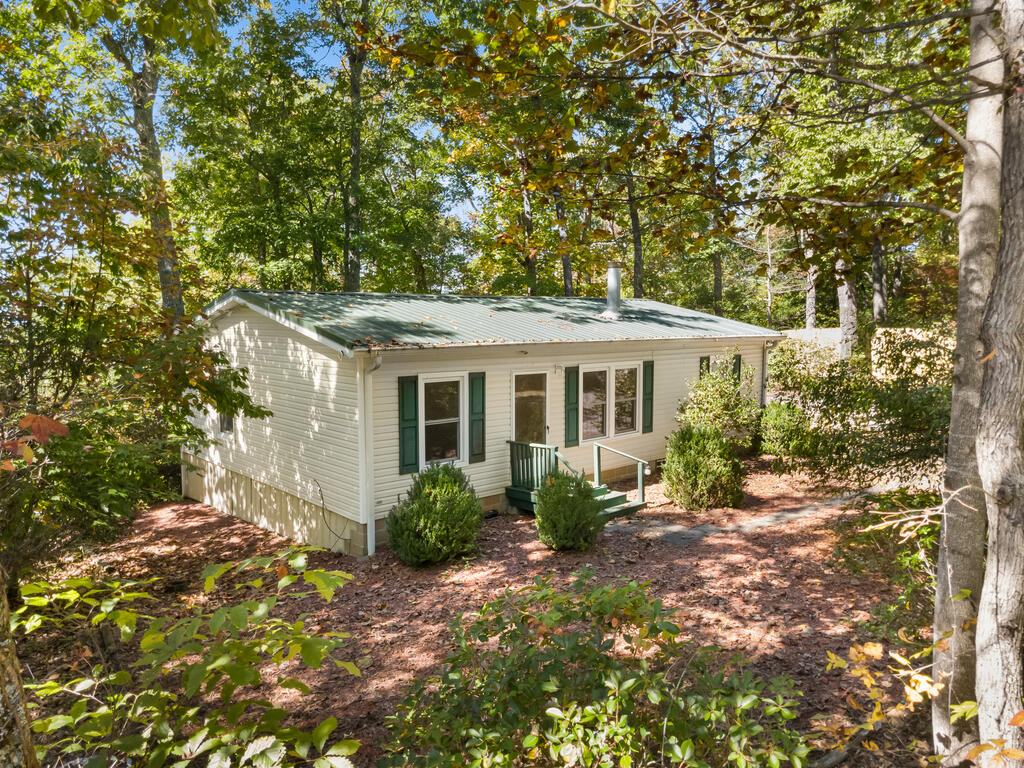 Single-story home with green shutters and metal roof nestled among autumn trees.