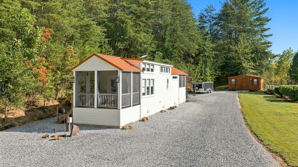 White manufactured home with a covered porch and orange roof beside a gravel driveway.