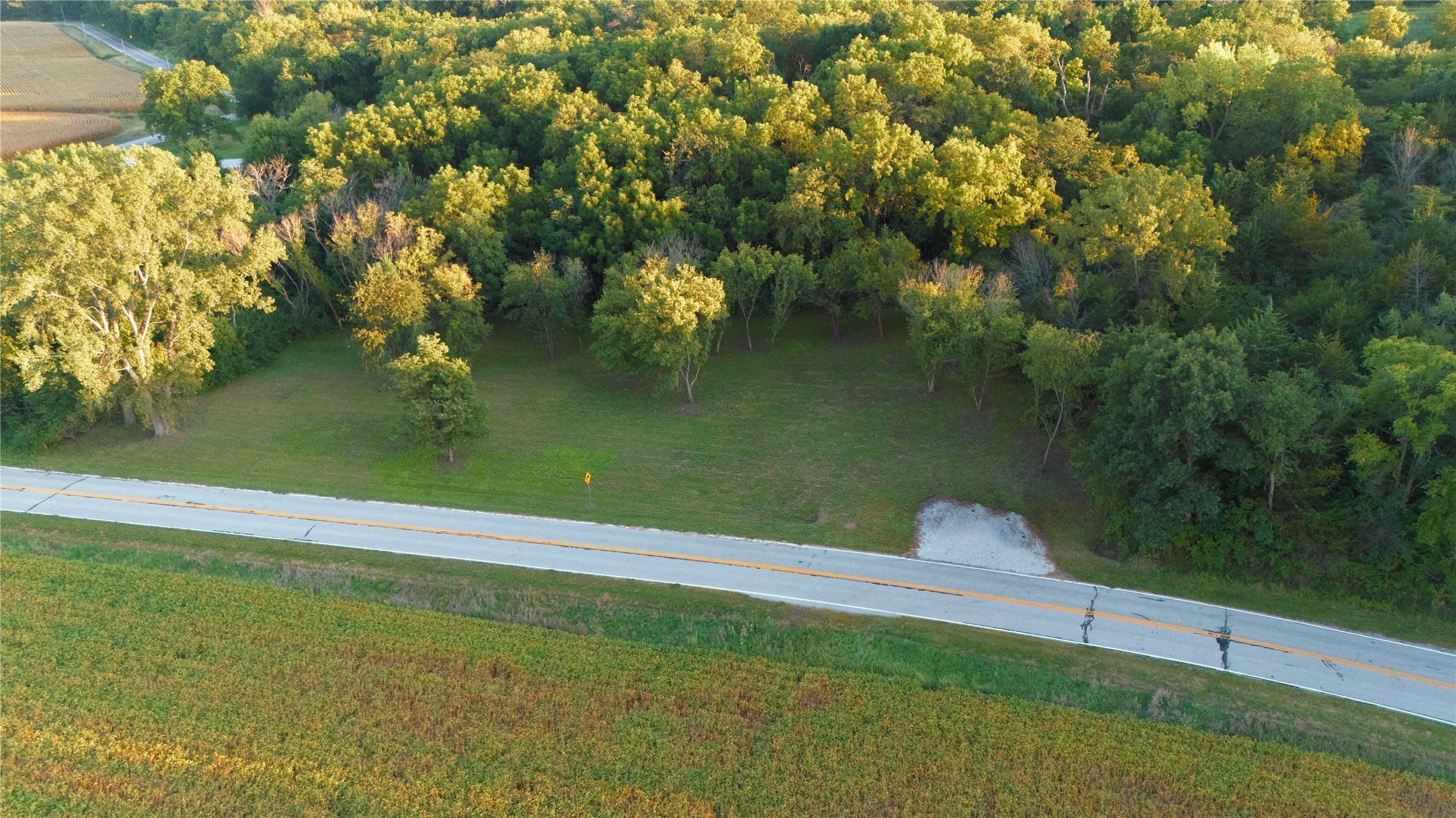 Aerial view of a wooded property with a grassy clearing and gravel entrance beside a road.