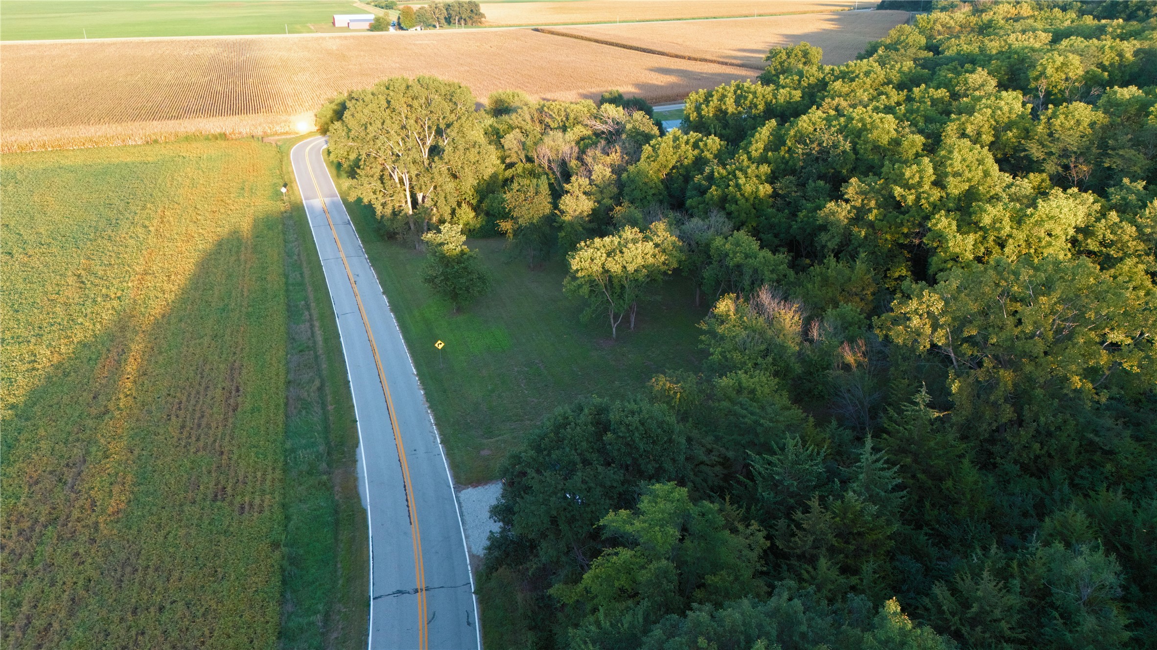 Aerial view of a country road bordered by farmland and dense woodland.
