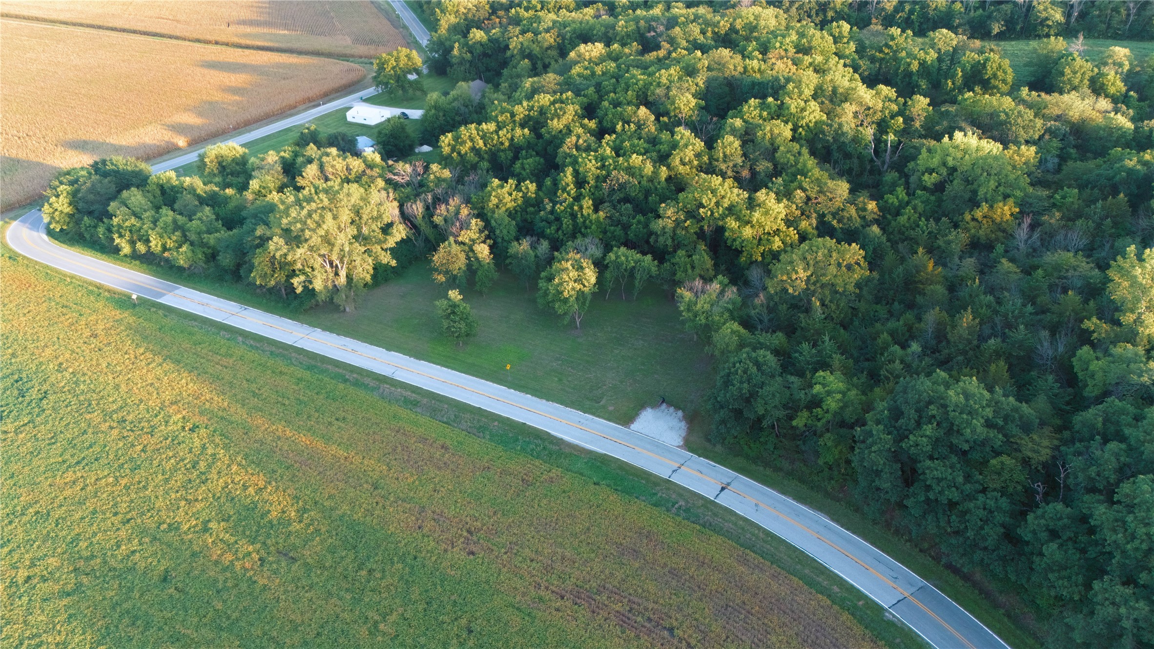 Aerial view of wooded land with a grassy clearing beside a curving rural road.
