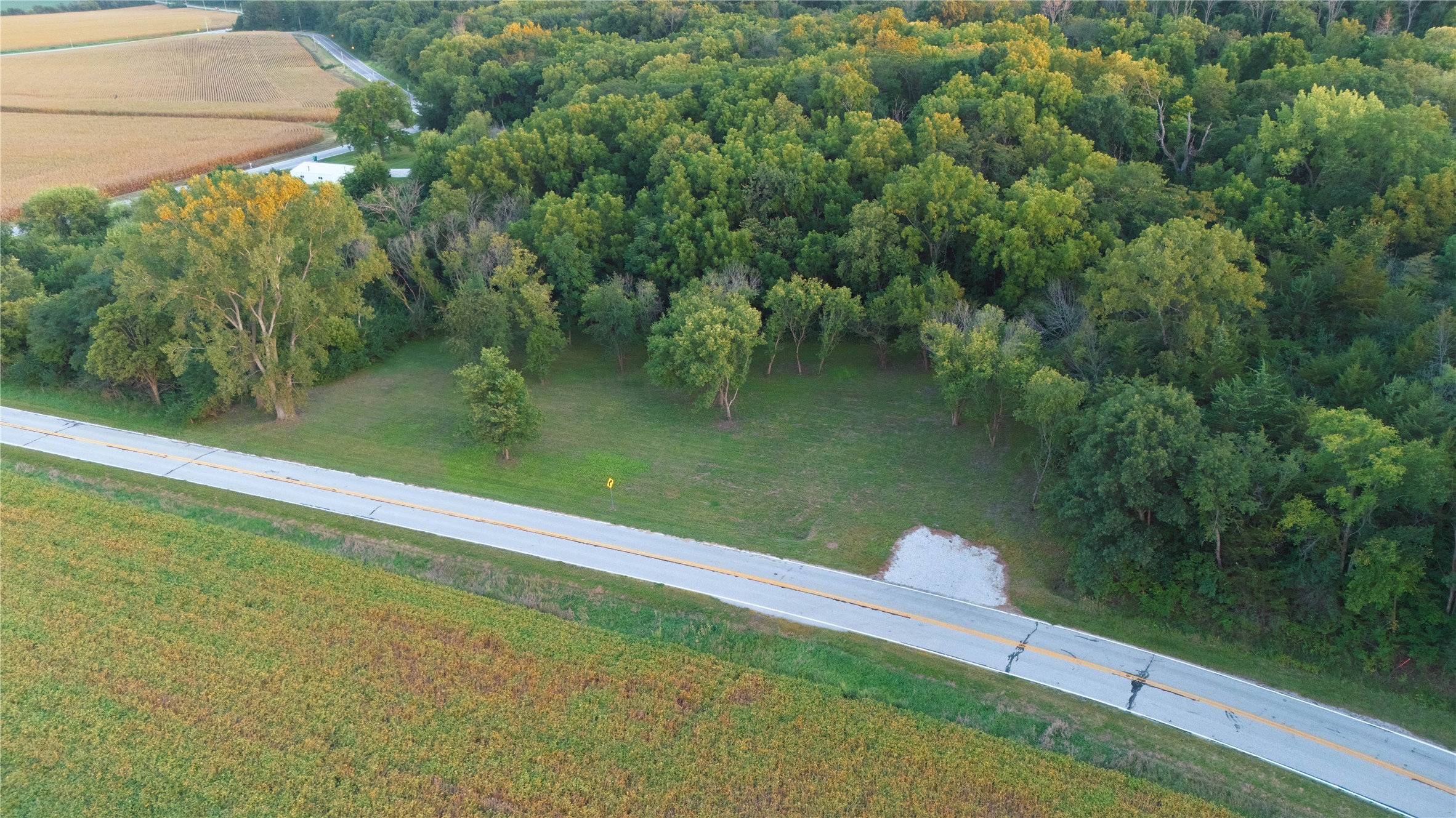 Aerial view of a wooded lot with a grassy clearing beside a two-lane road.