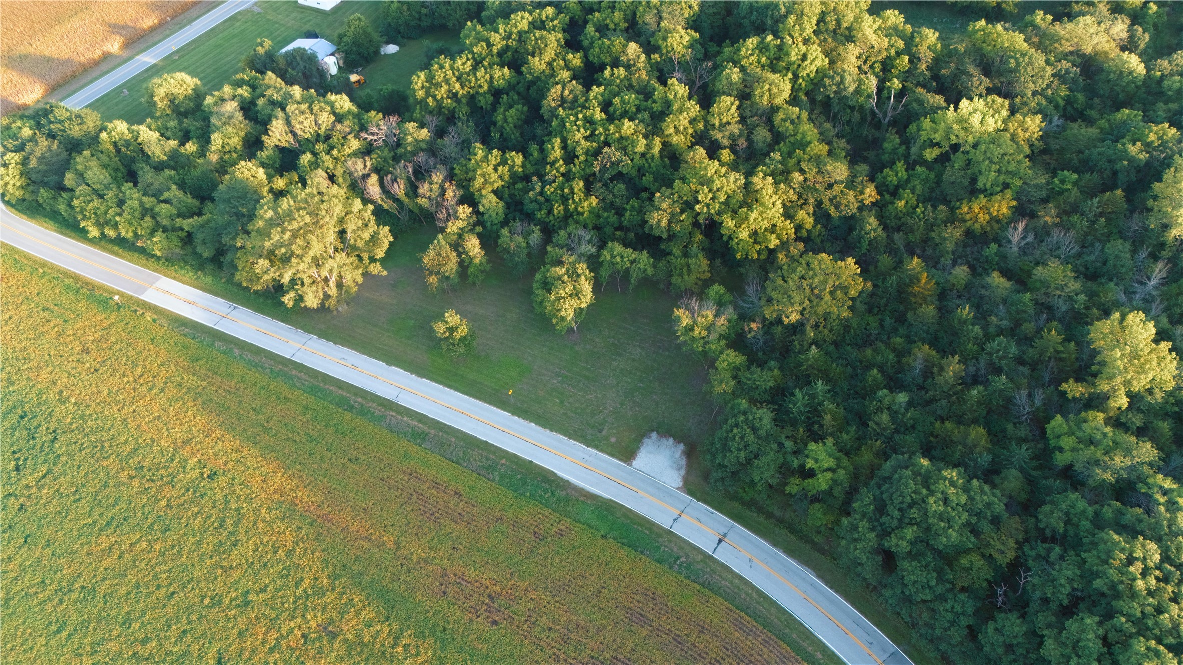 Aerial view of wooded acreage and grassy clearing beside a curving road.