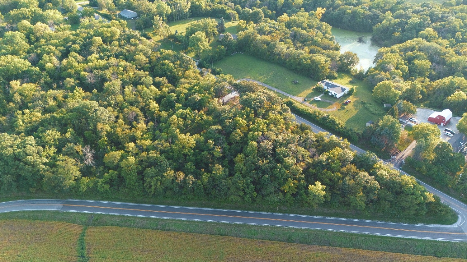 Aerial view of a wooded rural property with a white house, outbuildings, and a road curving along the tree line.