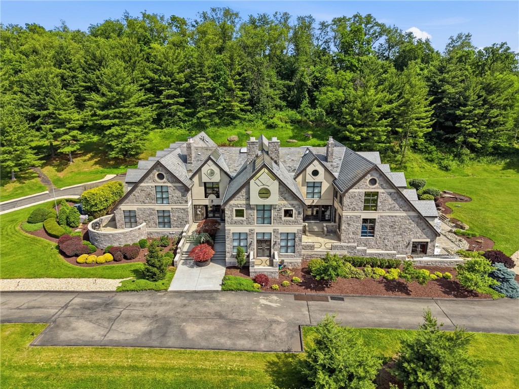 Aerial view of a large stone house with landscaped grounds and dense woods behind it.