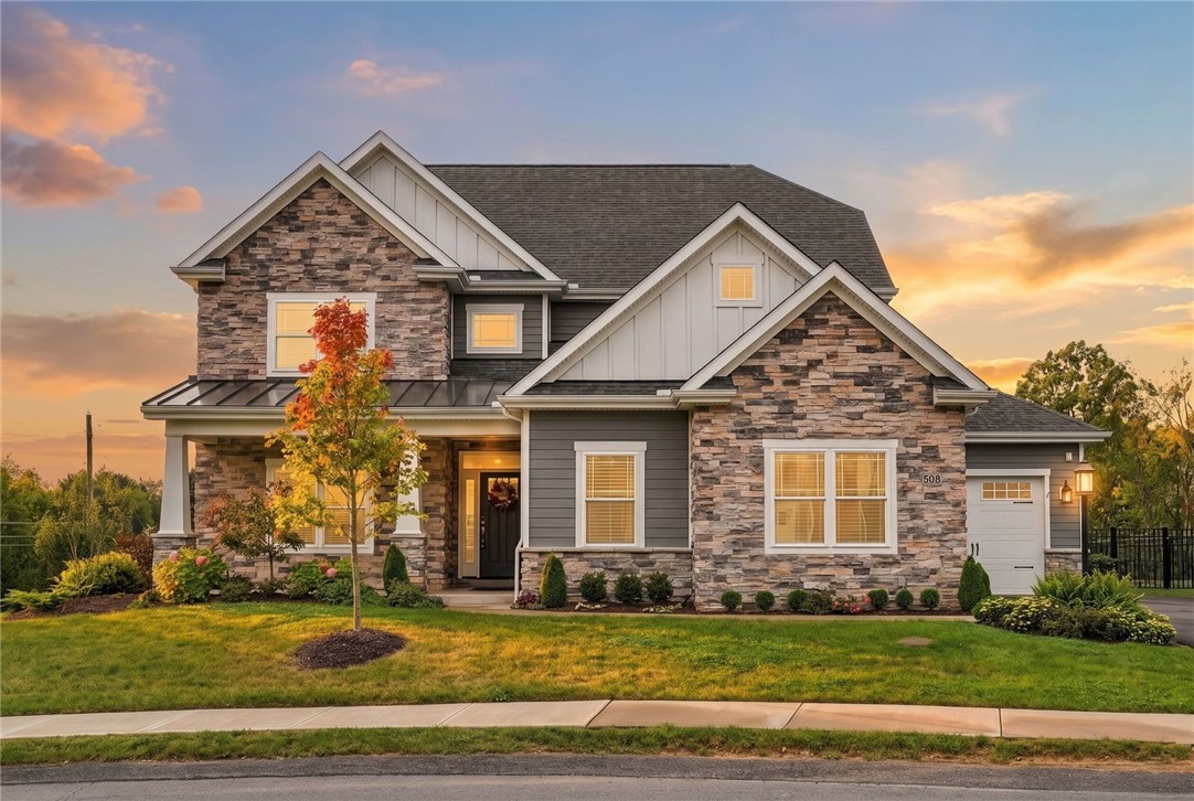 Two-story stone-and-gray-sided house with an attached garage and autumn landscaping at sunset.