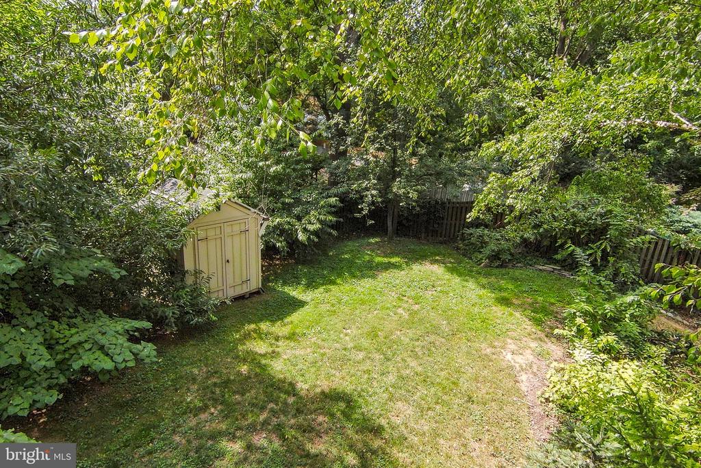 Backyard lawn with a beige storage shed, mature trees, and a wooden fence.