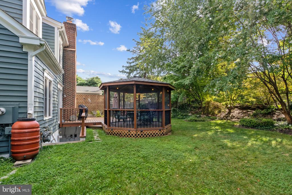 Backyard with a screened gazebo beside a small deck, surrounded by lawn and mature trees.