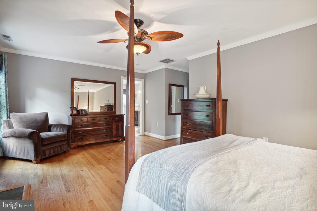 Bedroom with a large bed, dark wood dressers, hardwood floors, and a wooden-blade ceiling fan.