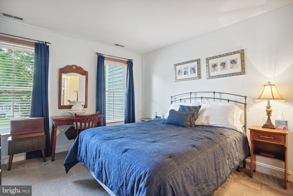 Bedroom with a large blue-covered bed, blue curtains, and a wooden vanity beside two windows.