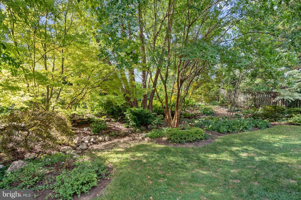 Landscaped backyard with a lawn, mature trees, stone garden border, and wooden fence.