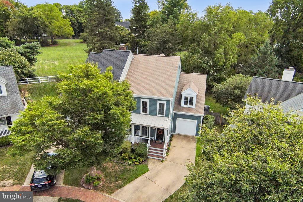 Aerial view of a blue-gray two-story home with a tan roof, front porch, and curved driveway.
